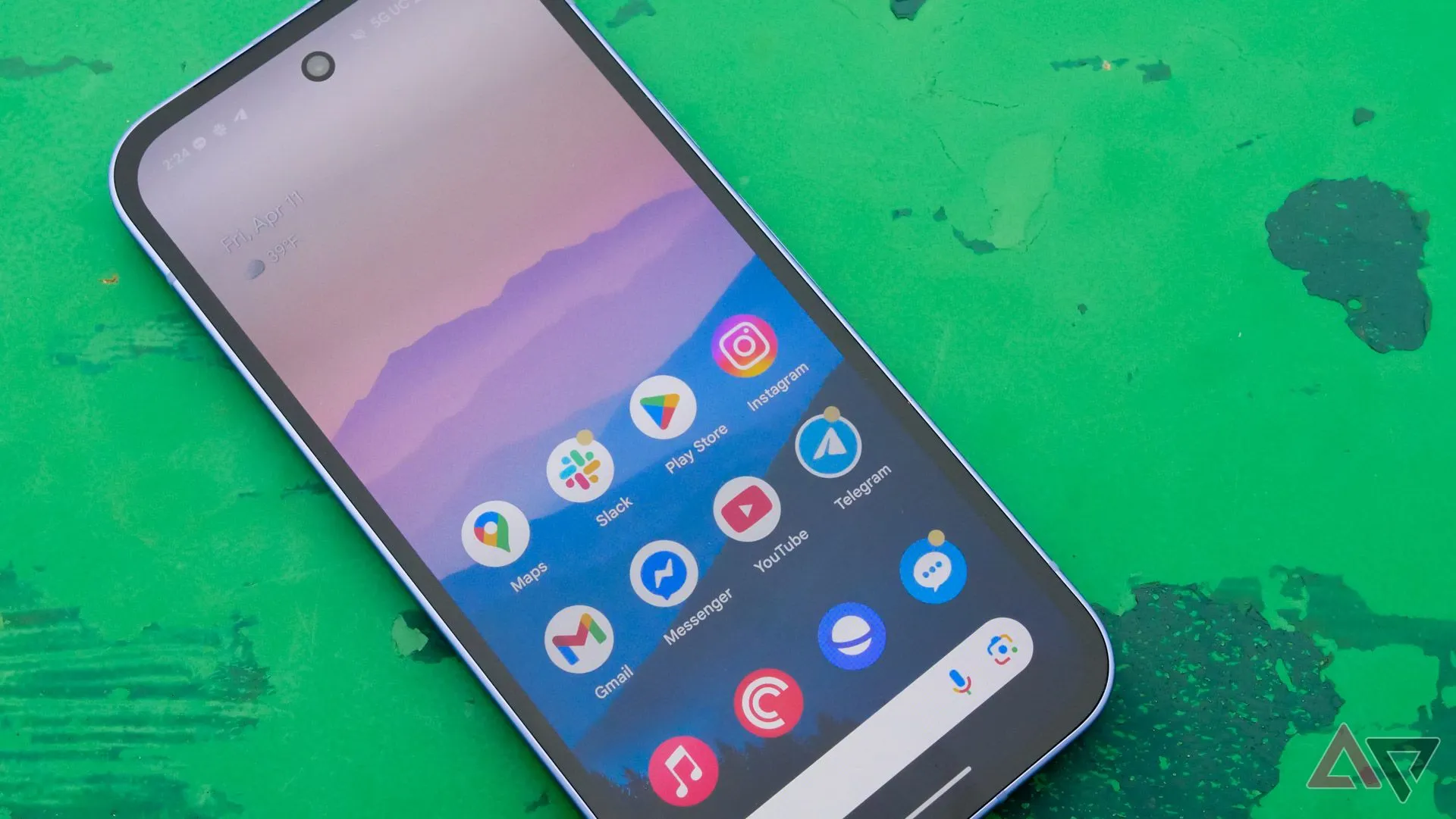 Điện thoại Pixel 9a đặt trên bàn xanh ngoài trời, hiển thị màn hình sống động