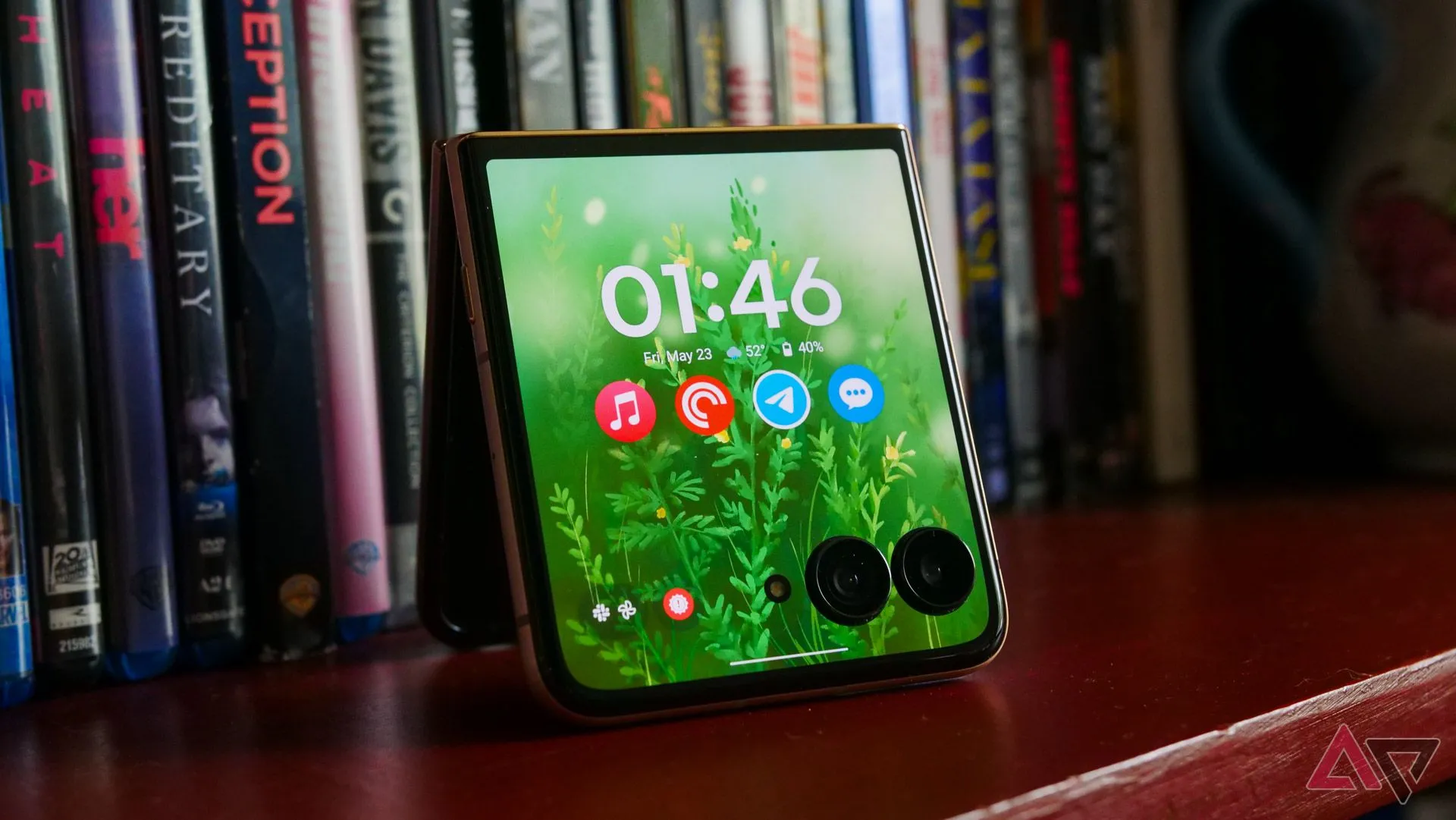 Mặt trước điện thoại Motorola Razr Ultra (2025) với màn hình phụ hiển thị đang đặt trên giá sách gỗ.