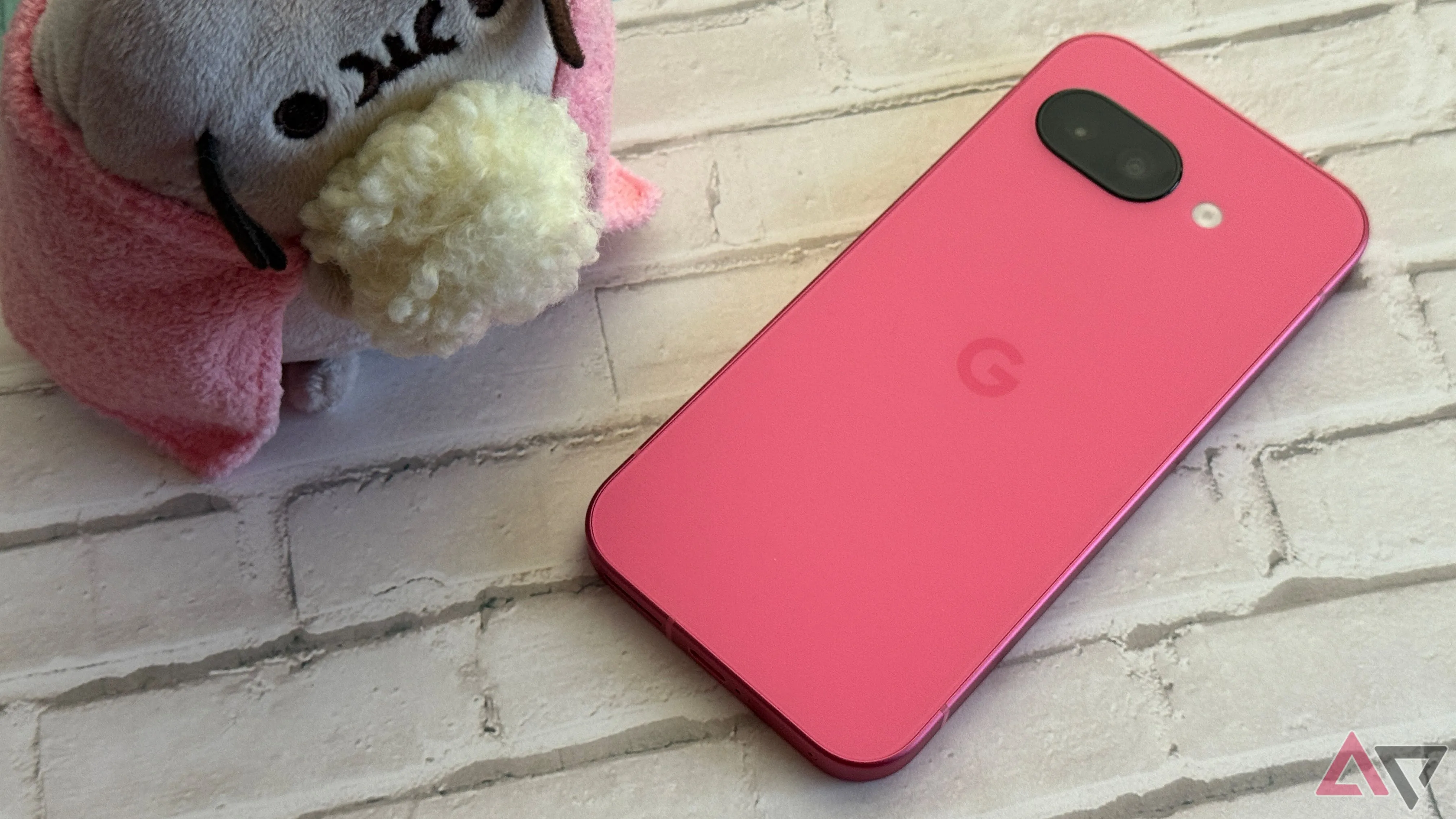 Pixel 9a phiên bản màu Peony (hồng) đặt cạnh vật trang trí, thể hiện kích thước nhỏ gọn