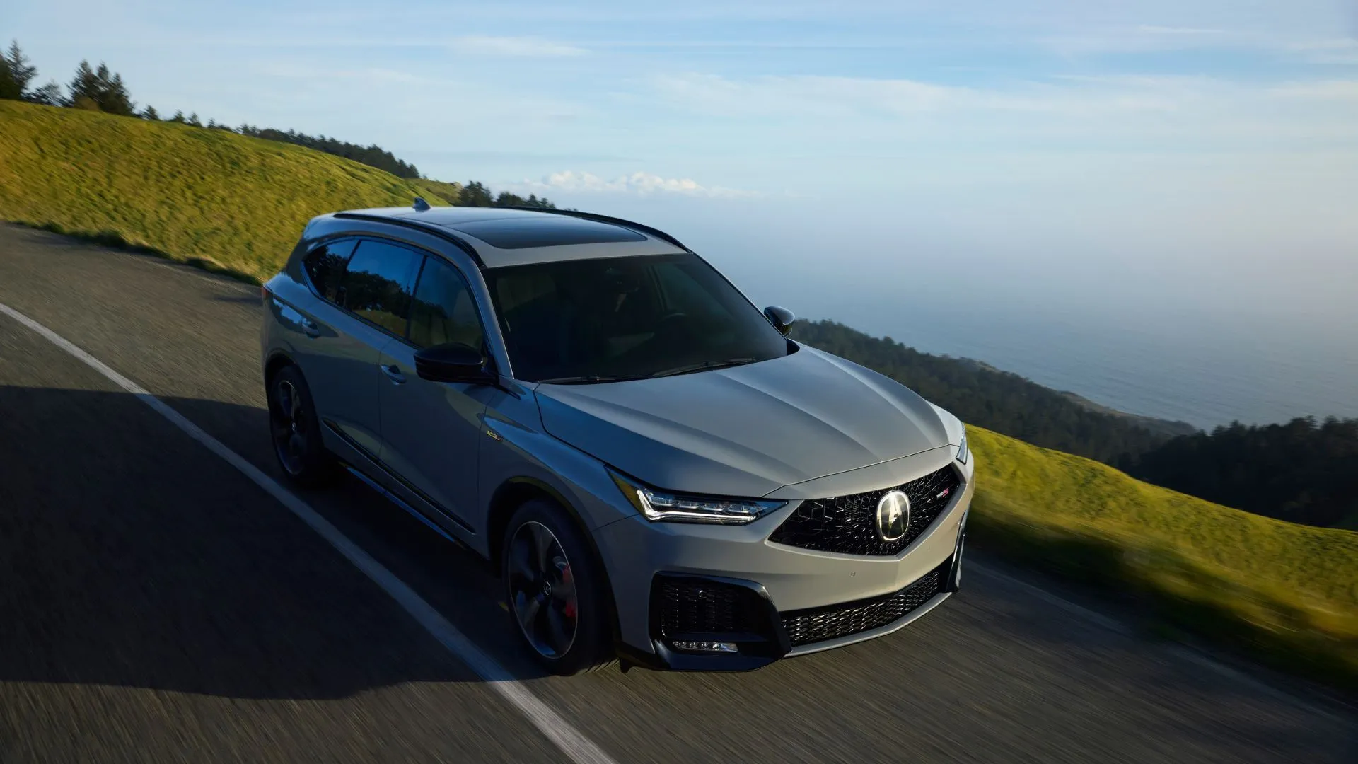 Acura MDX Type S 2025 màu xám mạnh mẽ đang chạy trên con đường nông thôn, toát lên vẻ thể thao và sang trọng.