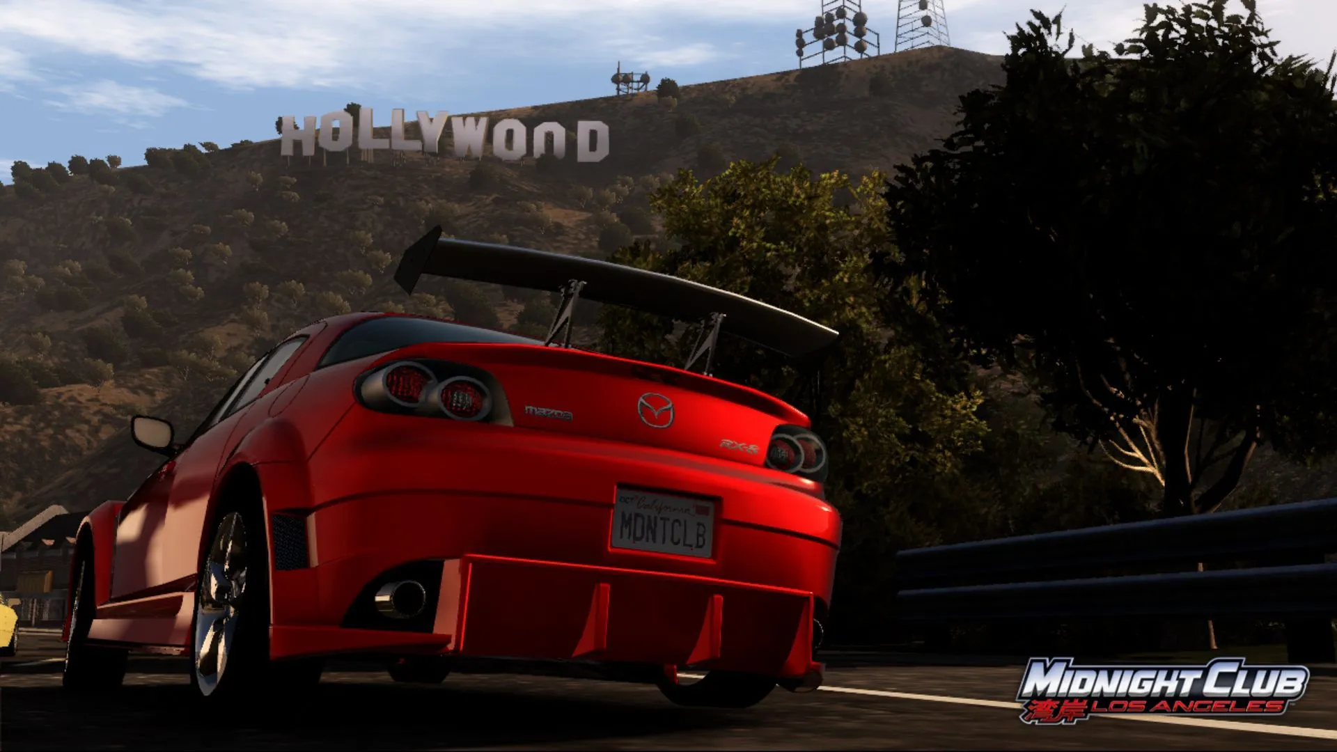 Ảnh chụp màn hình từ Midnight Club: Los Angeles với chiếc Mazda màu cam trên đường, phía sau là biểu tượng Hollywood