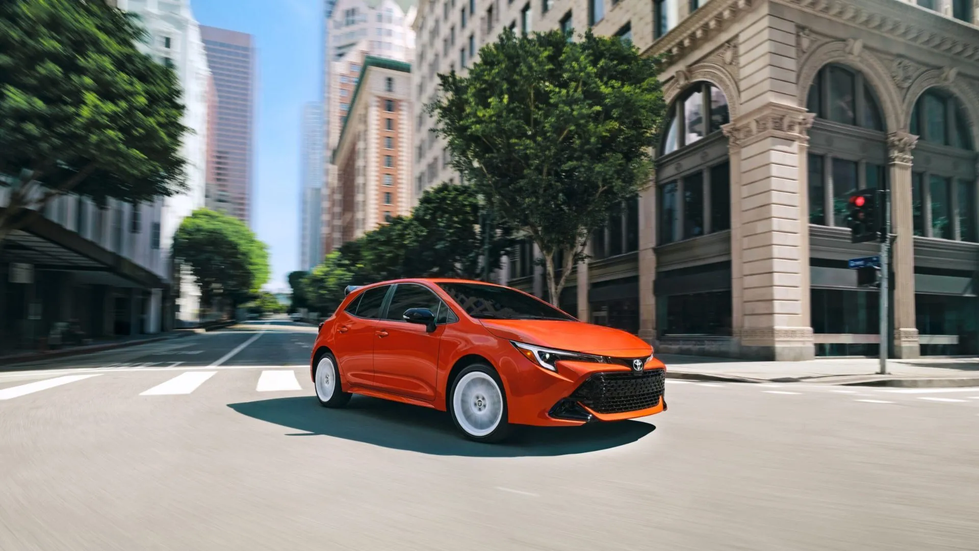 Ảnh động ba phần tư phía trước của một chiếc Corolla Hatchback FX Edition 2026 màu cam đang lái qua thành phố.
