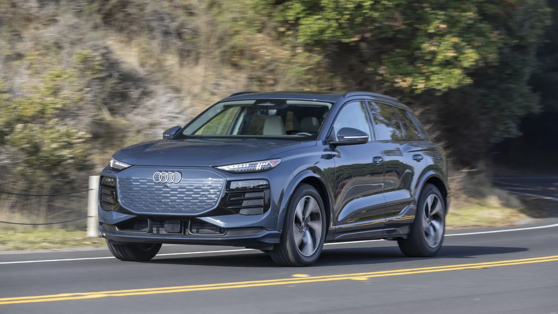 Audi Q6 e-tron 2025 màu xanh ngọc di chuyển trên con đường nông thôn, đại diện cho các mẫu xe điện cao cấp chịu ảnh hưởng bởi chính sách tín dụng thuế EV.