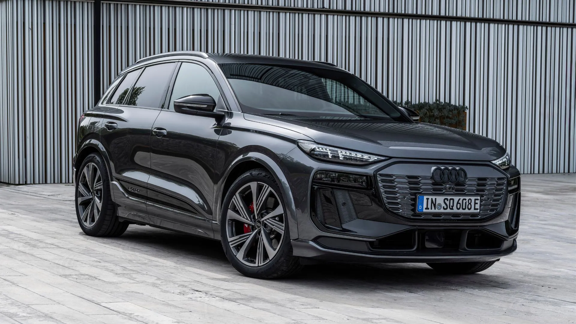 Audi SQ6 e-tron 2025 màu xám đang đỗ bên ngoài một tòa nhà hiện đại, thể hiện thiết kế tinh tế và hiệu suất điện mạnh mẽ.