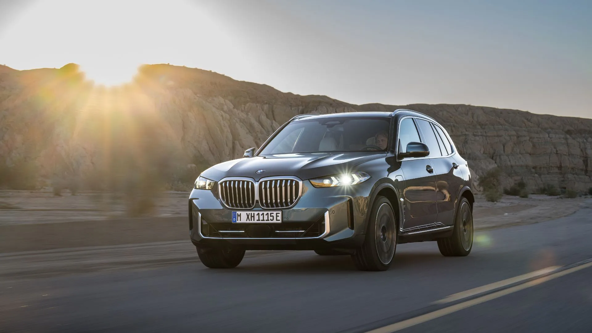 BMW X5 xDrive50e 2024 màu xanh lam đang chạy trên con đường nông thôn trong ánh hoàng hôn, thể hiện sự kết hợp hoàn hảo giữa hiệu suất và hiệu quả.