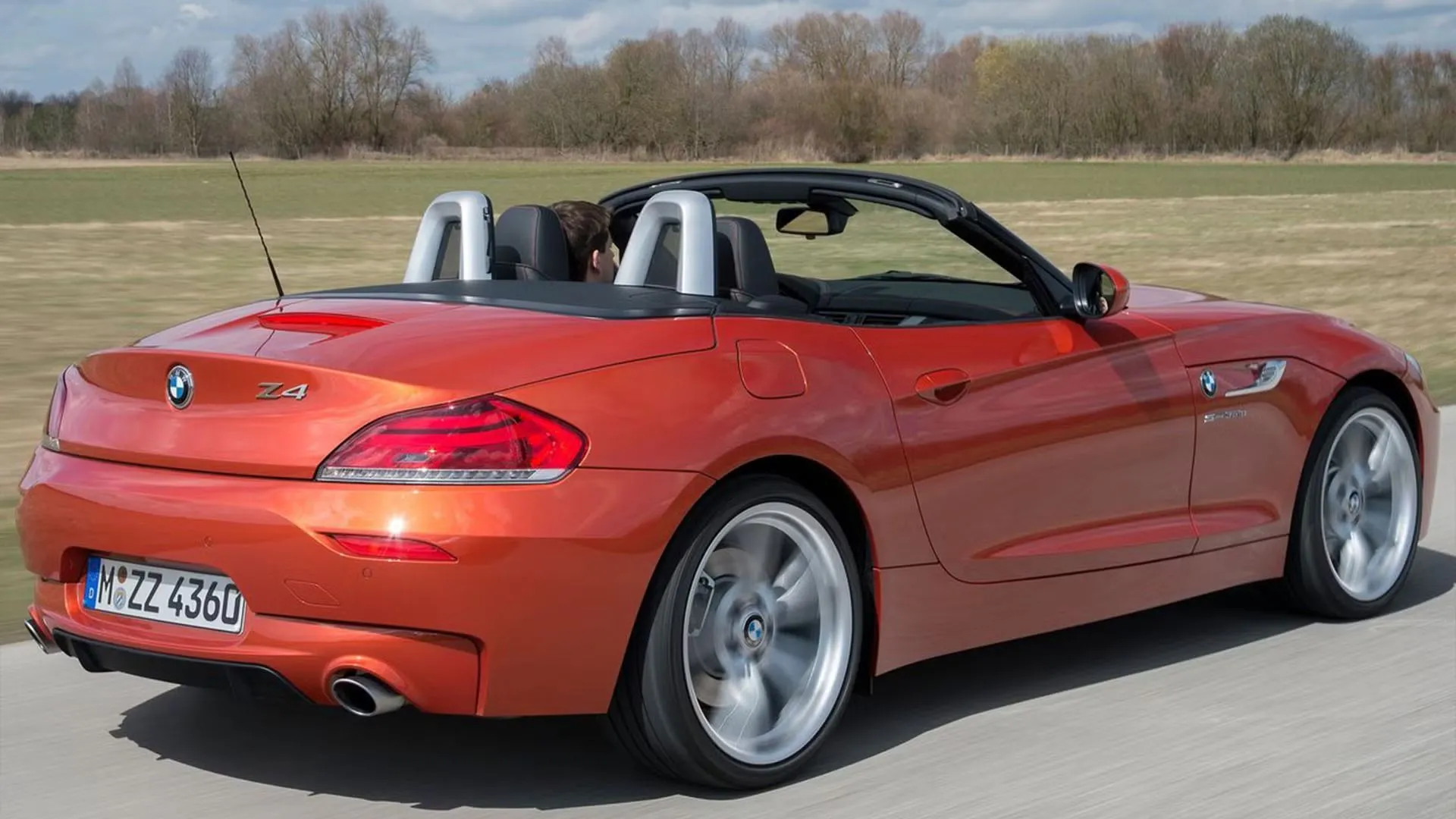 BMW Z4 màu cam đang chạy trên đường nông thôn với mui hạ