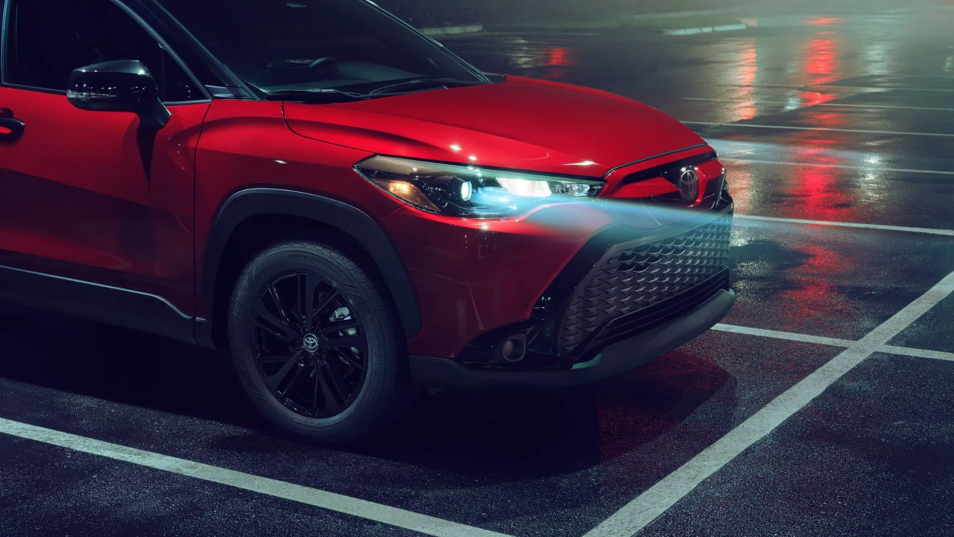 Cận cảnh đầu xe của Toyota Corolla Cross Nightshade 2024 màu đỏ vào ban đêm với đèn pha sáng rõ