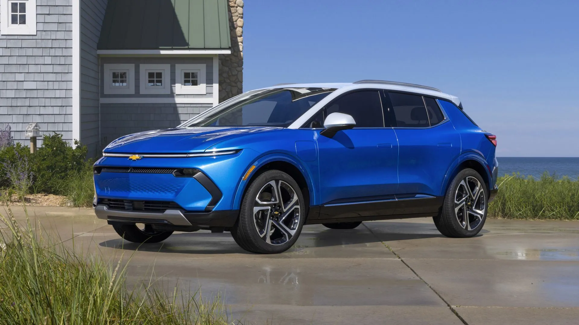 Chevrolet Equinox EV 2025 màu xanh đậu trước nhà gần biển, tượng trưng cho mẫu SUV điện đa dụng và giá cả phải chăng.