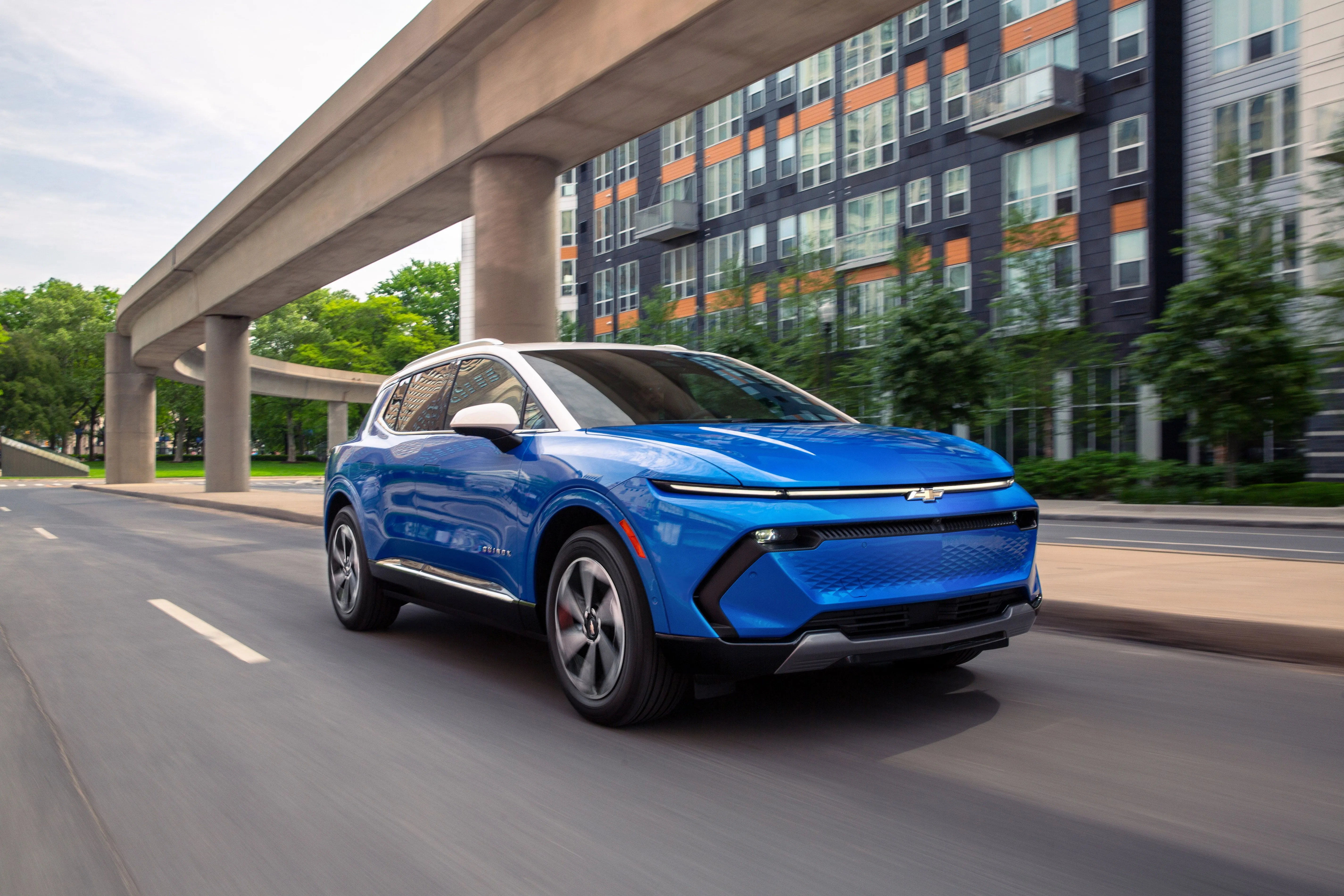 Chevrolet Equinox EV màu xanh lam lướt đi trong thành phố, đại diện cho xe điện giá phải chăng