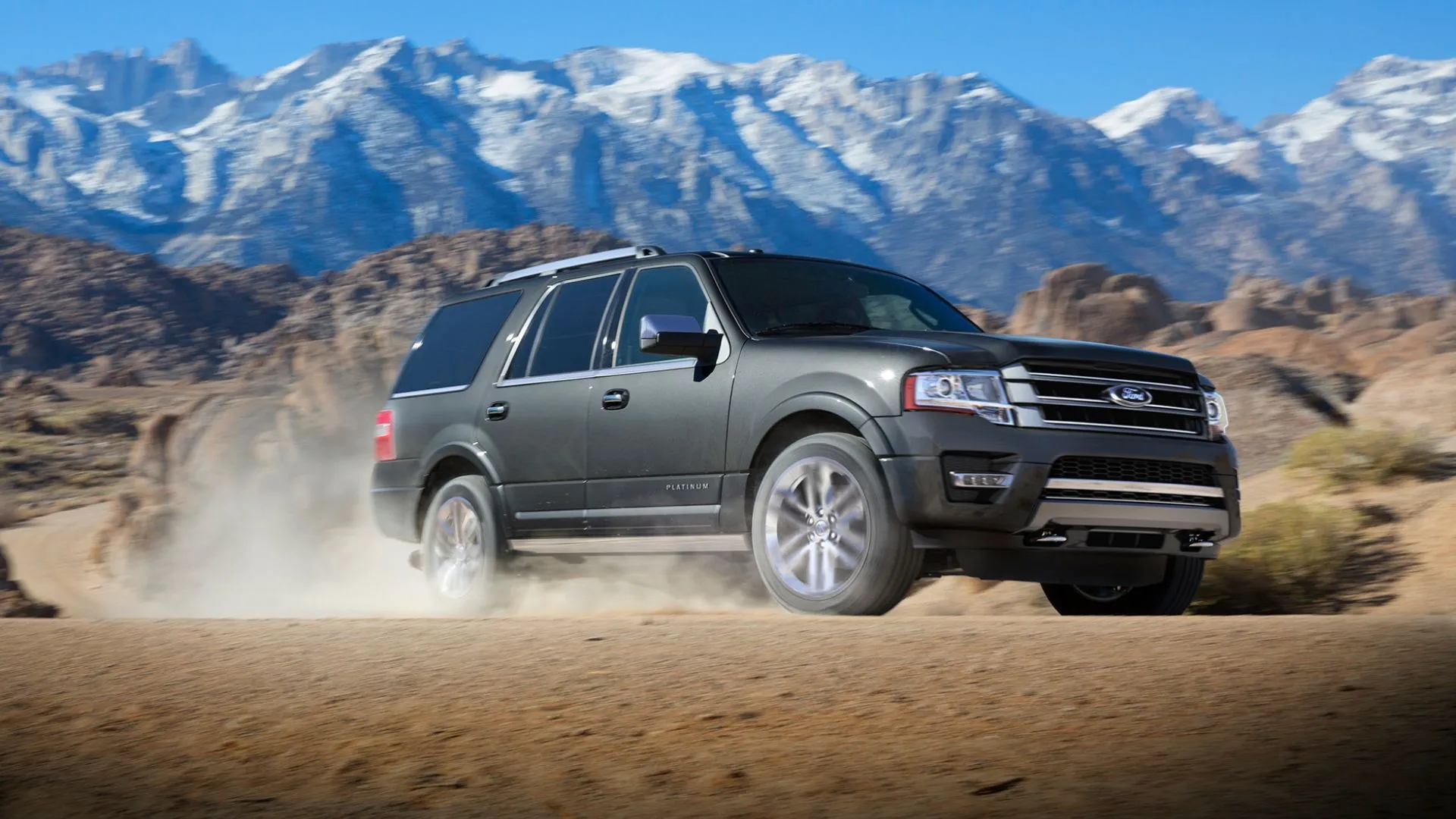 Chiếc Ford Expedition Platinum 2017 màu xám đang vượt địa hình cát với núi phủ tuyết phía sau