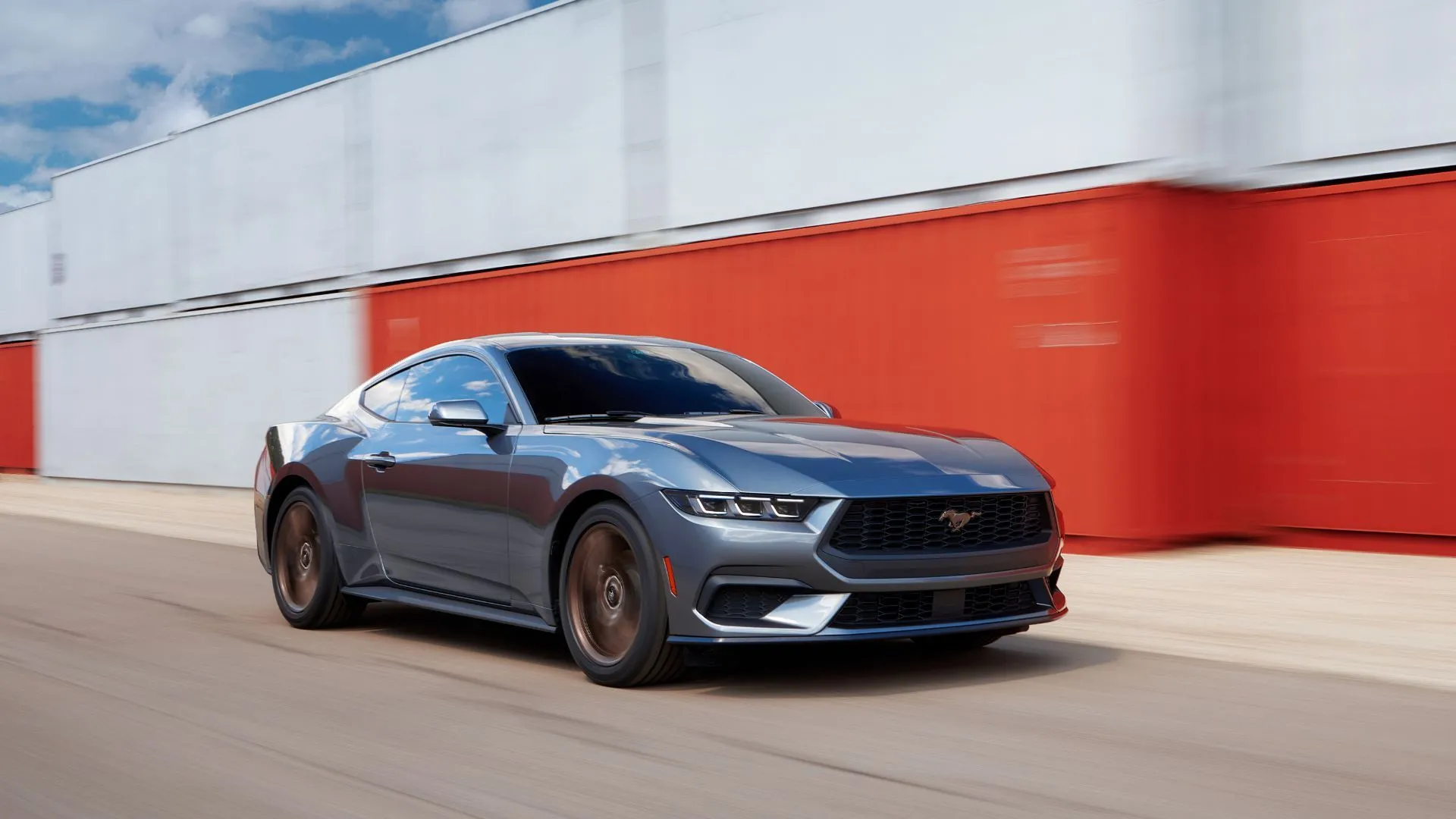 Chiếc Ford Mustang 2024 màu xám di chuyển qua hàng container