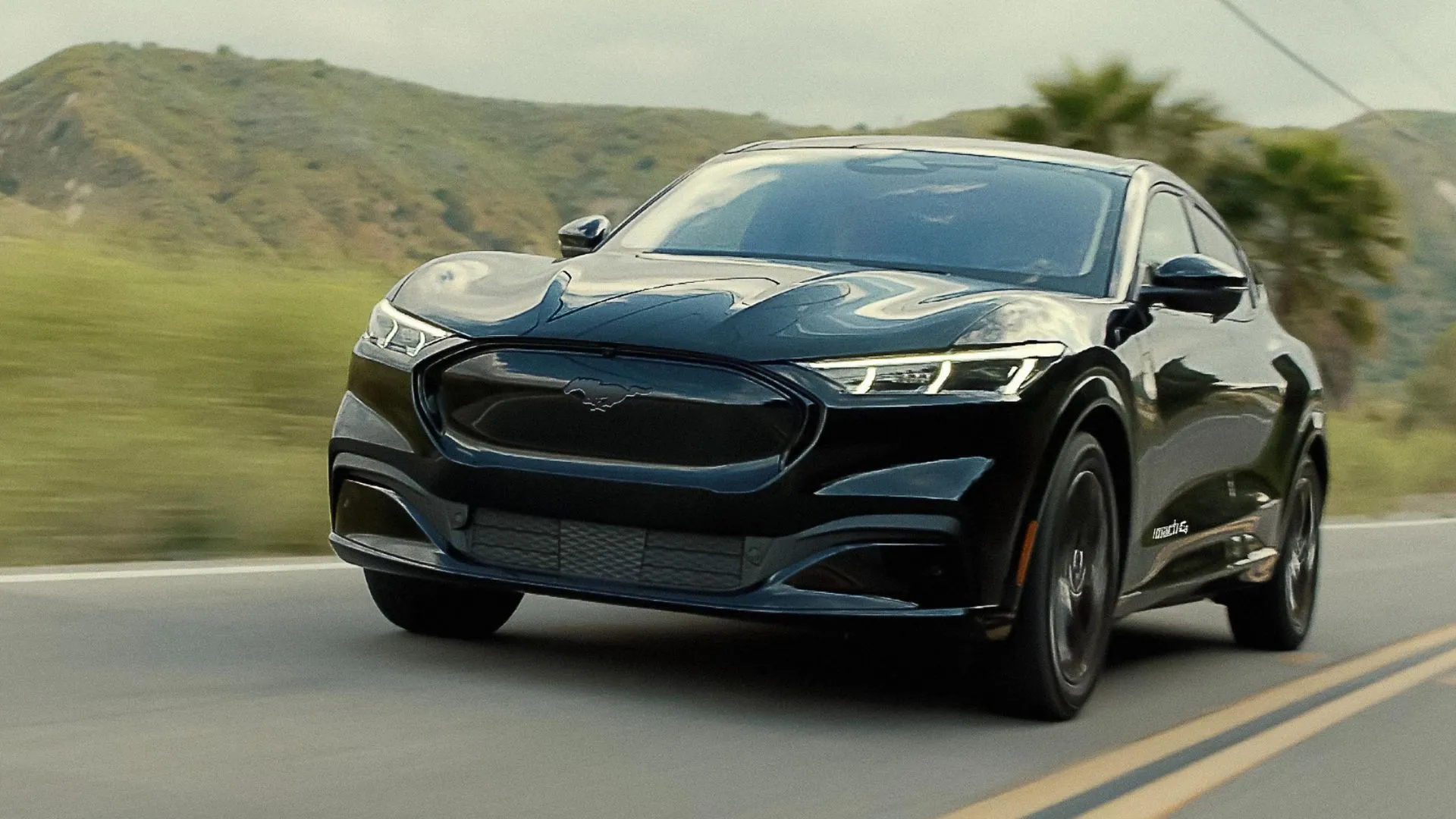 Chiếc SUV điện Ford Mustang Mach-E 2025 màu đen đang chạy trên đường nông thôn, tích hợp công nghệ BlueCruise.