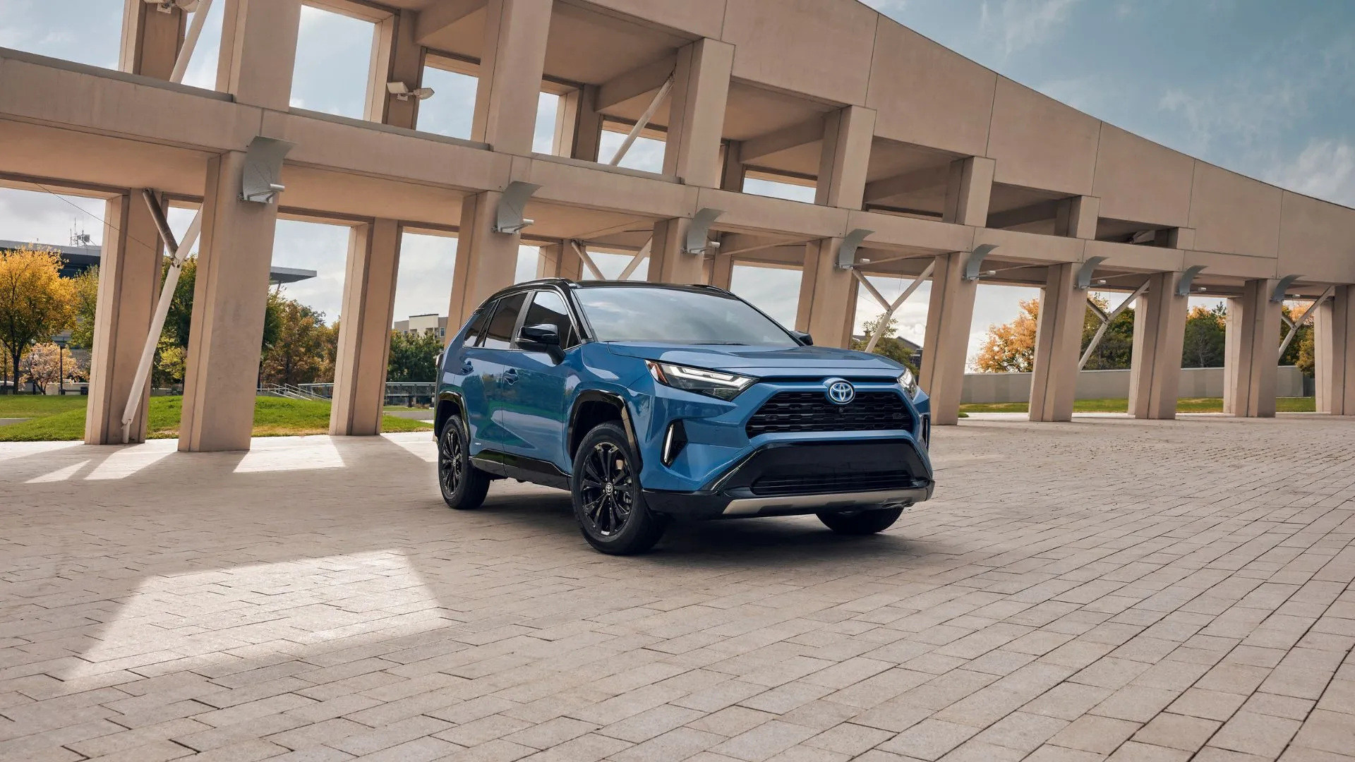 Chiếc Toyota RAV4 Hybrid XSE 2024 màu xanh dương đỗ trên nền đá cuội, cho thấy sự kết hợp giữa thiết kế đô thị và khả năng vận hành vượt trội.