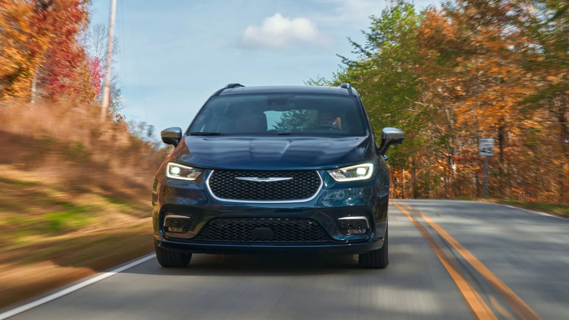 Đầu xe Chrysler Pacifica PHEV Pinnacle 2025 màu xanh đậm trên đường có cây