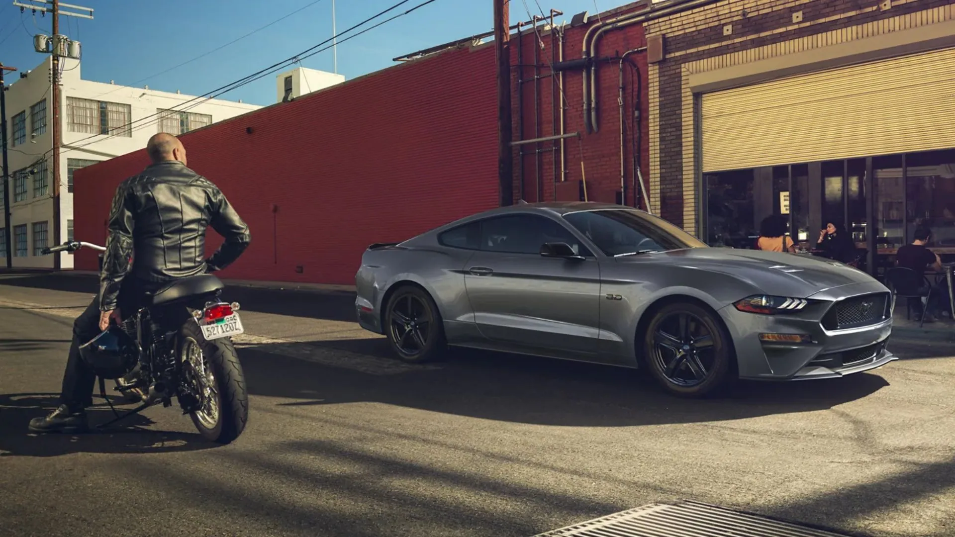 Ford Mustang GT màu đen được trưng bày bên cạnh một người đàn ông trên xe máy