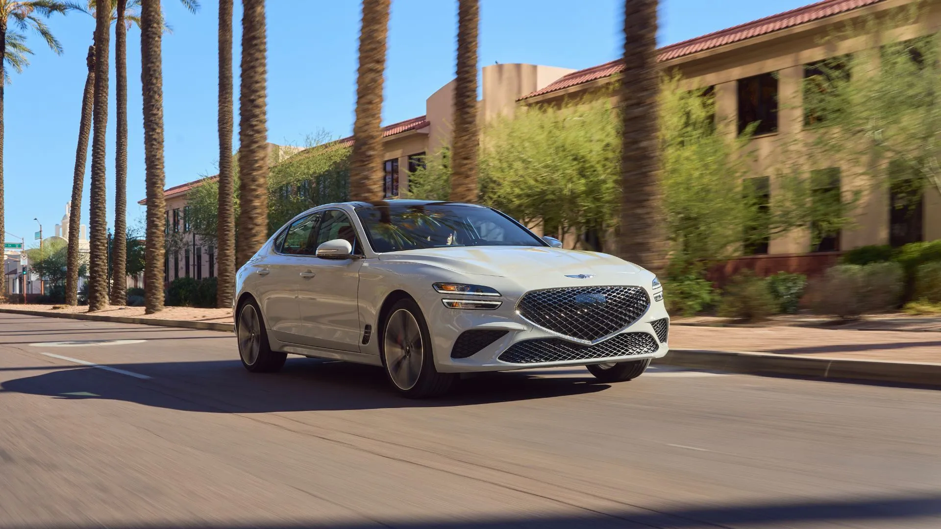Genesis G70 2025 màu xám bạc lướt qua thành phố đầy cọ, thể hiện sự sang trọng và khả năng đỗ xe thông minh