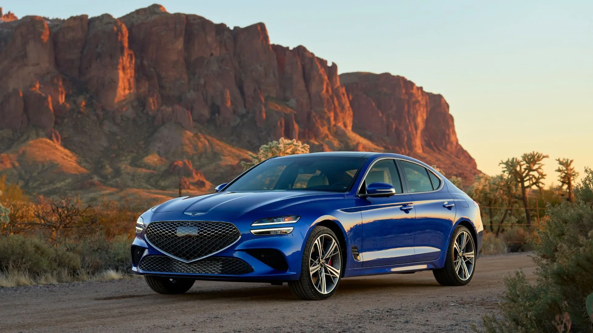 Genesis G70 đời 2025 màu xanh lam cá tính đang đậu trên nền đá sỏi với núi non phía sau