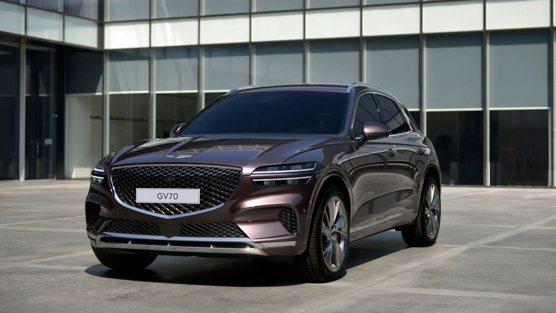 Genesis GV70 thế hệ đầu tiên màu tím đang đỗ bên ngoài một tòa nhà hiện đại, thể hiện sự sang trọng và tinh tế của thương hiệu.