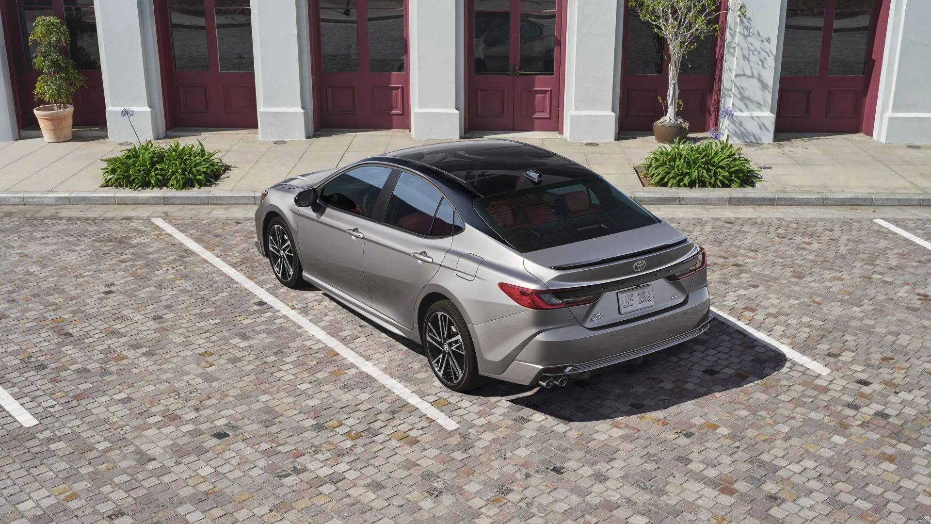 Góc 3/4 phía sau của Toyota Camry Hybrid XSE 2025 màu xám đậu bên ngoài một tòa nhà hiện đại