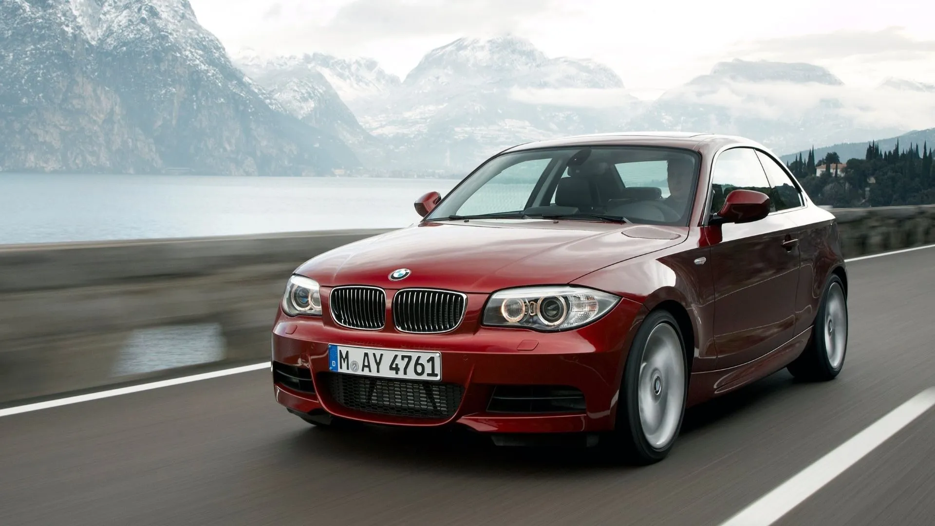 Góc 3/4 phía trước của một chiếc BMW 1-Series Coupe màu trắng đời 2012 đang di chuyển trên đường, thể hiện sự nhỏ gọn và năng động đặc trưng của dòng xe coupe Đức.
