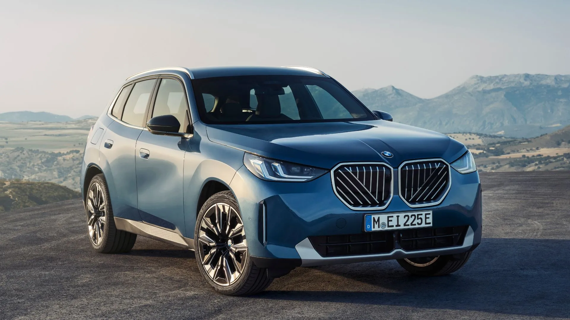 Góc 3/4 phía trước của một chiếc BMW X3 2025 màu xanh dương đỗ trên nền sỏi