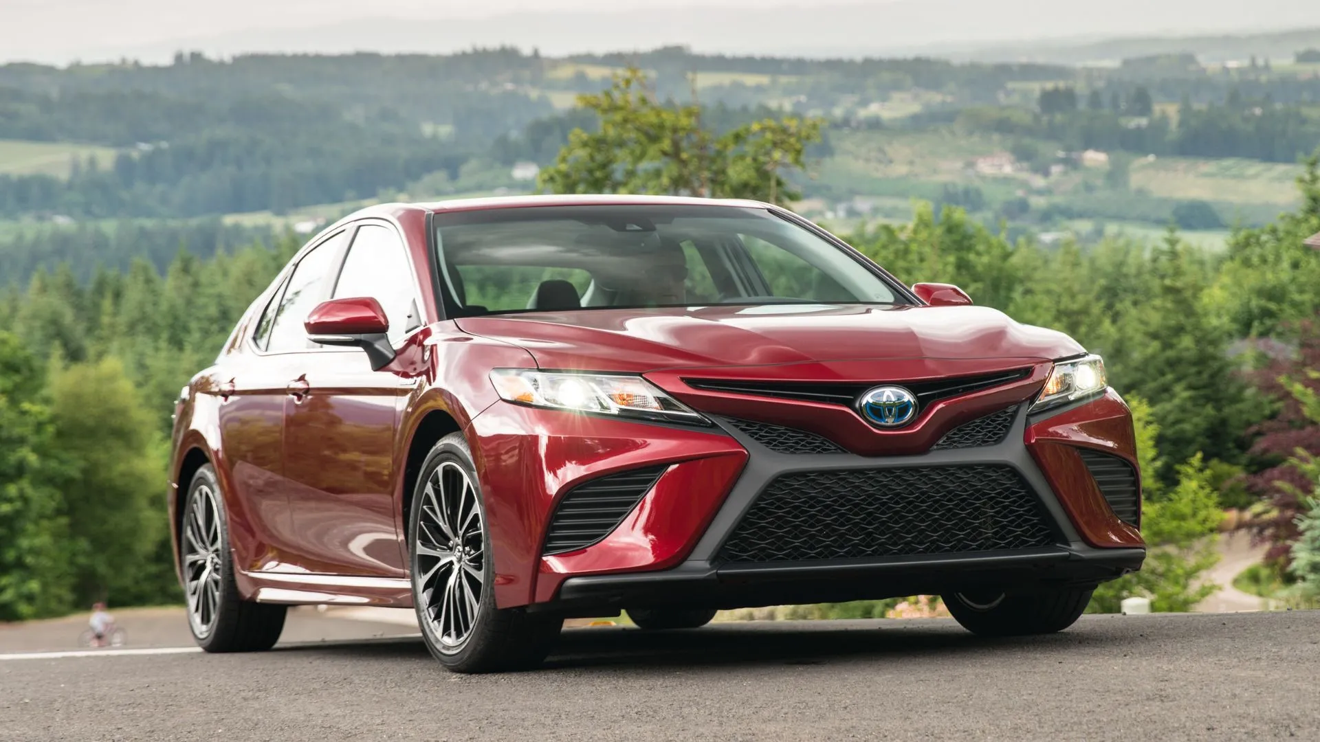 Góc 3/4 phía trước của một chiếc Toyota Camry SE Hybrid 2020 màu đỏ với cánh đồng làm nền