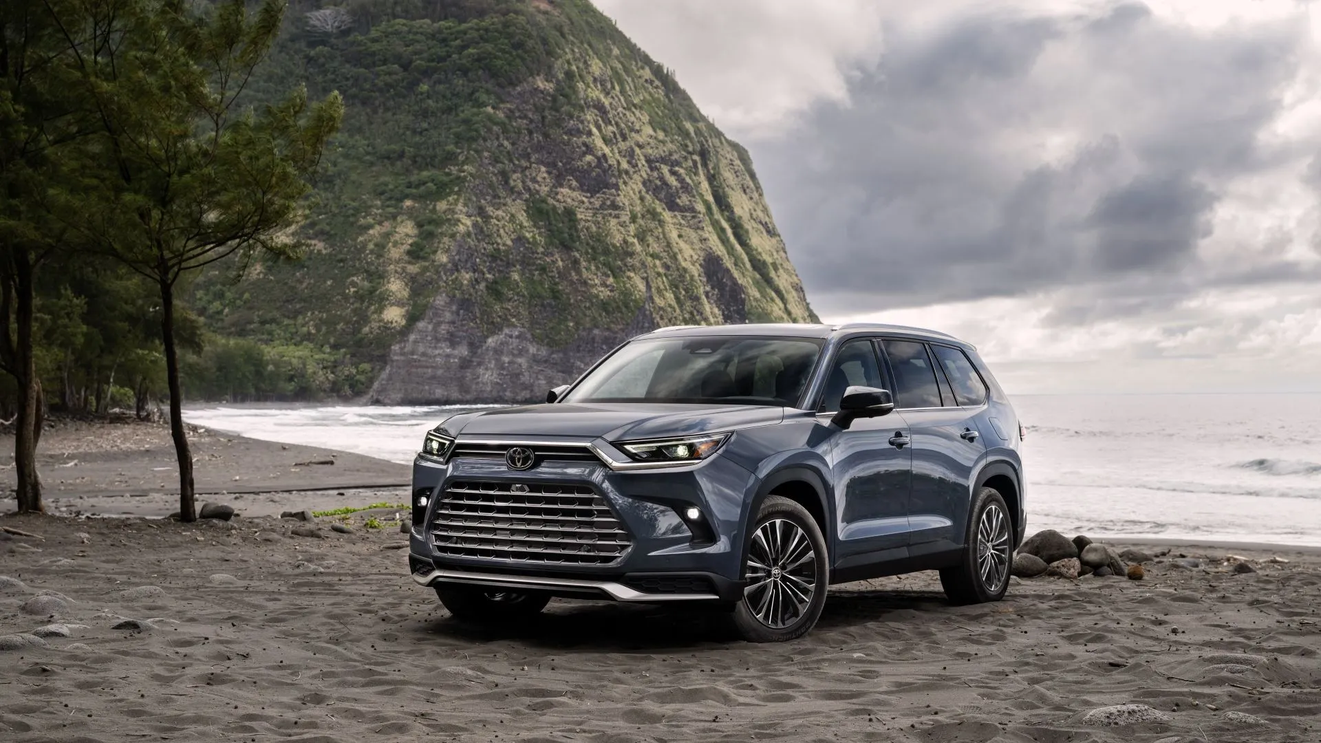 Góc 3/4 phía trước của Toyota Grand Highlander 2025 màu xám tro đỗ ngoài trời, mẫu SUV 3 hàng ghế rộng rãi.