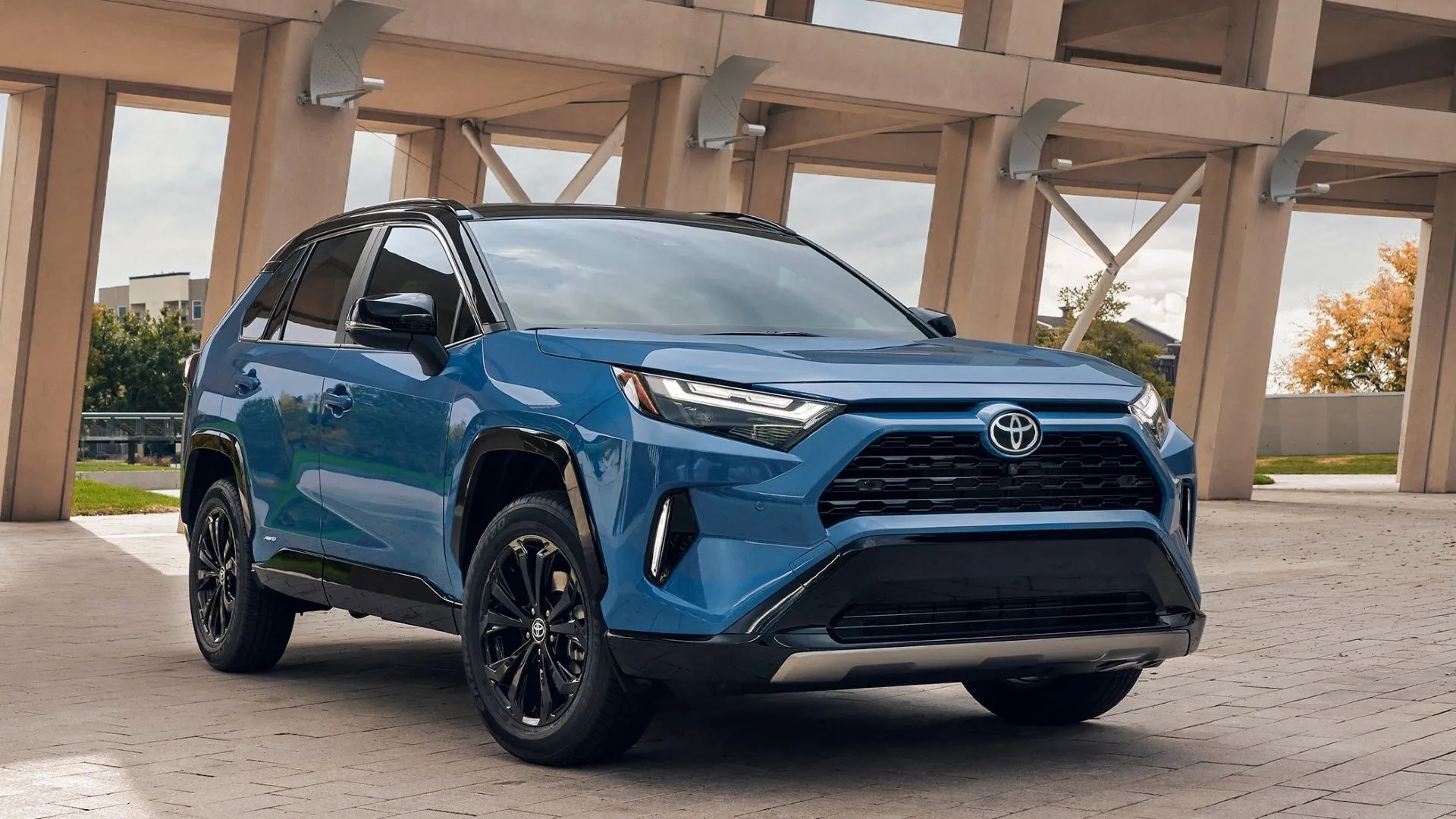 Góc 3/4 phía trước của xe SUV Toyota RAV4 Hybrid 2025 màu xanh đậu bên đường