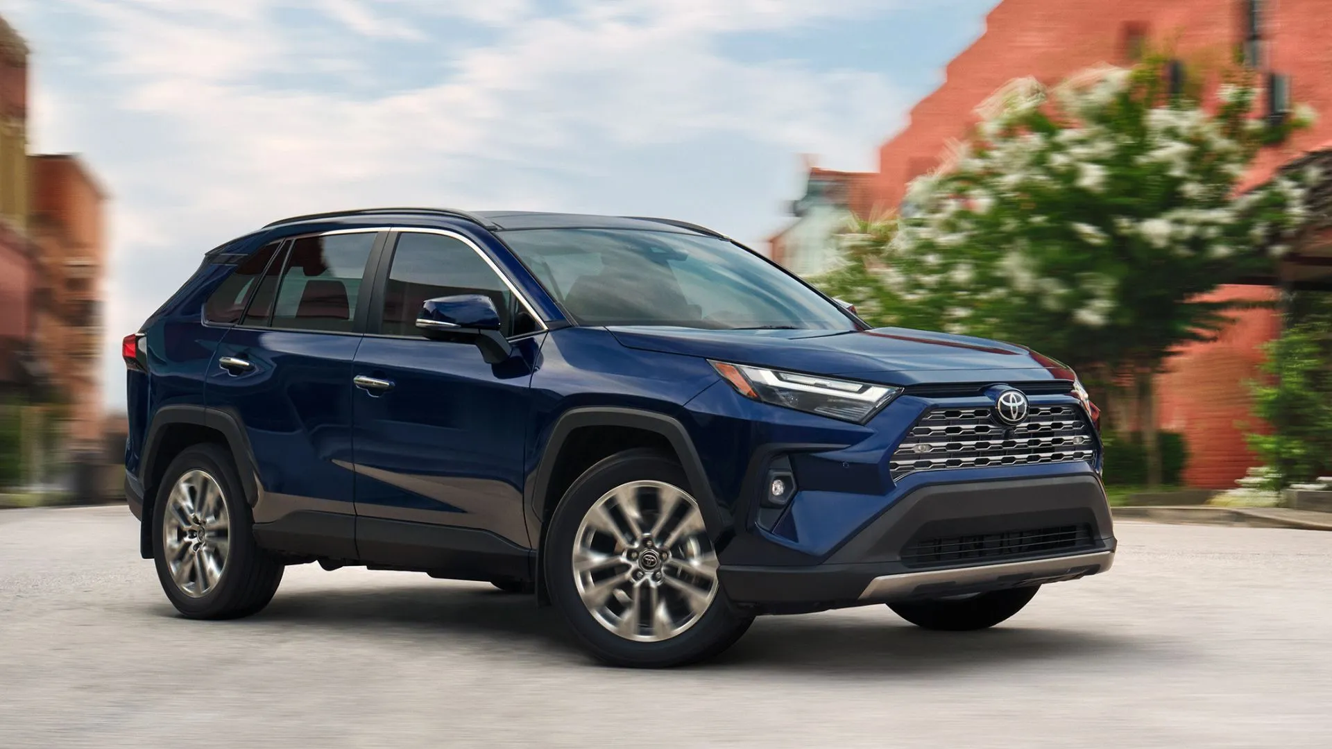 Góc 3/4 phía trước của xe SUV Toyota RAV4 LE 2025 màu xanh dương đang di chuyển trên đường phố.