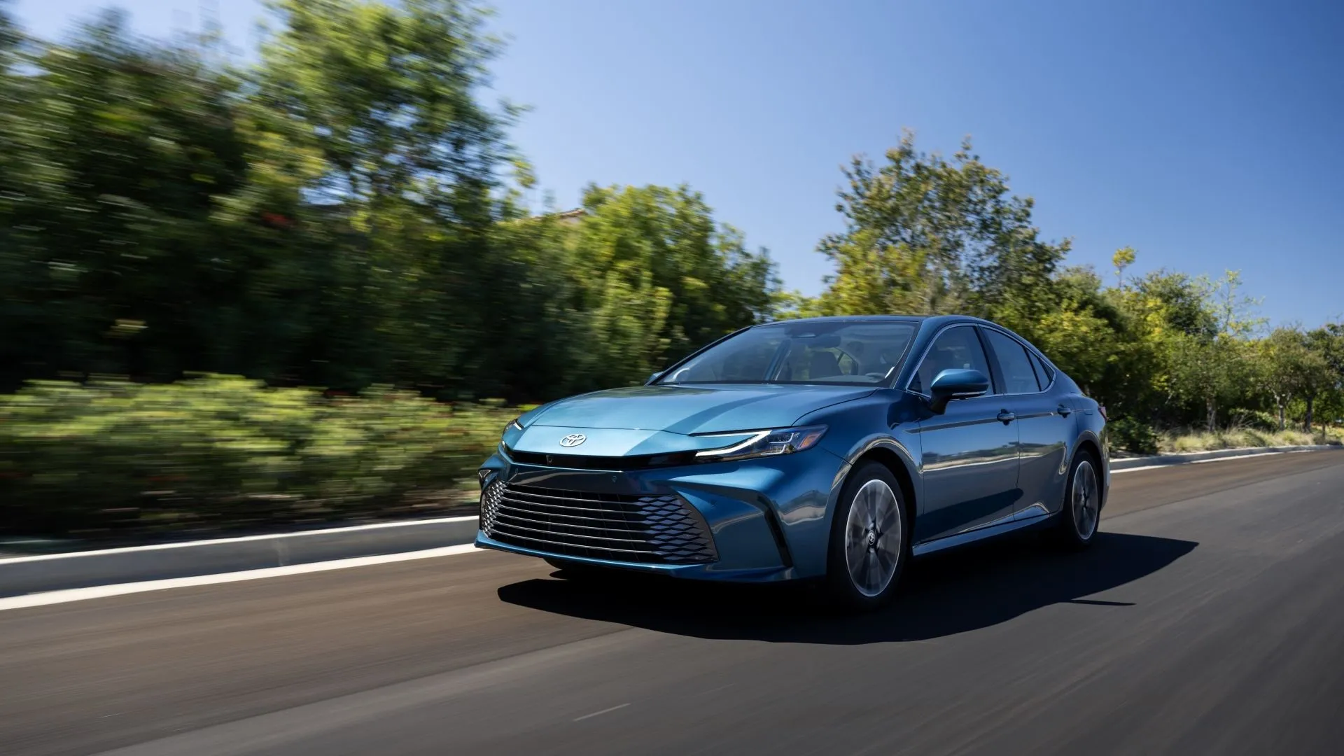 Góc 3/4 xe Toyota Camry Hybrid 2025 màu xanh ngọc đang di chuyển trên đường, thể hiện sự linh hoạt