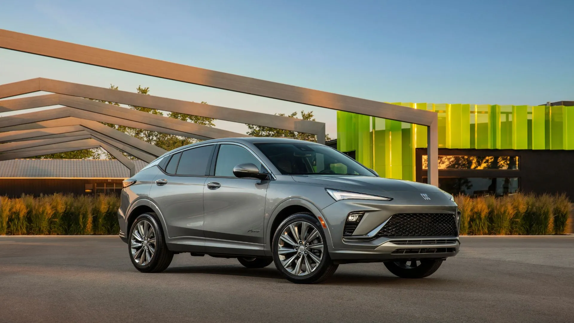 Góc ba phần tư phía trước của Buick Envista Avenir 2024 màu xám đỗ giữa các cấu trúc kiến trúc hiện đại, thể hiện thiết kế sang trọng và đô thị.