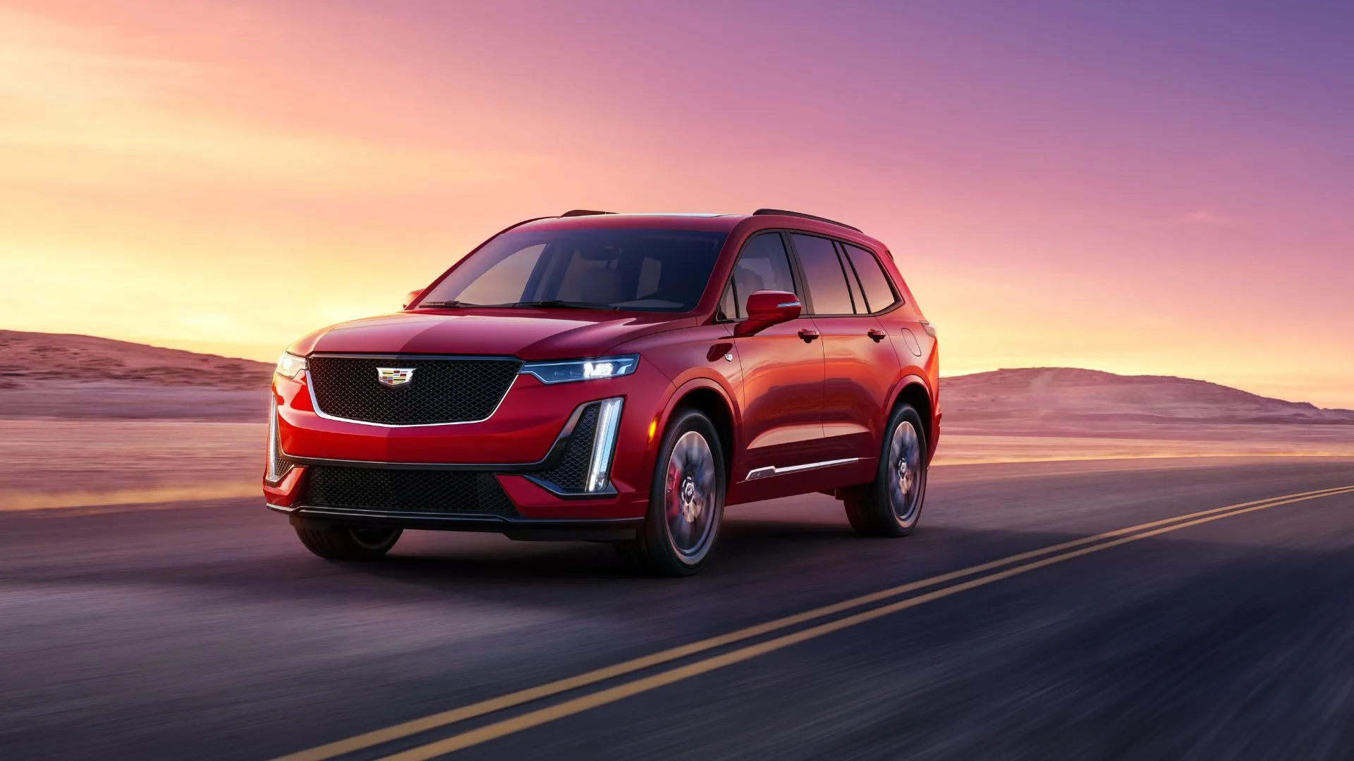Góc ba phần tư phía trước của Cadillac XT6 2024 màu đỏ đang lái trên đường xuyên qua sa mạc, thể hiện sự sang trọng và khả năng di chuyển ấn tượng.