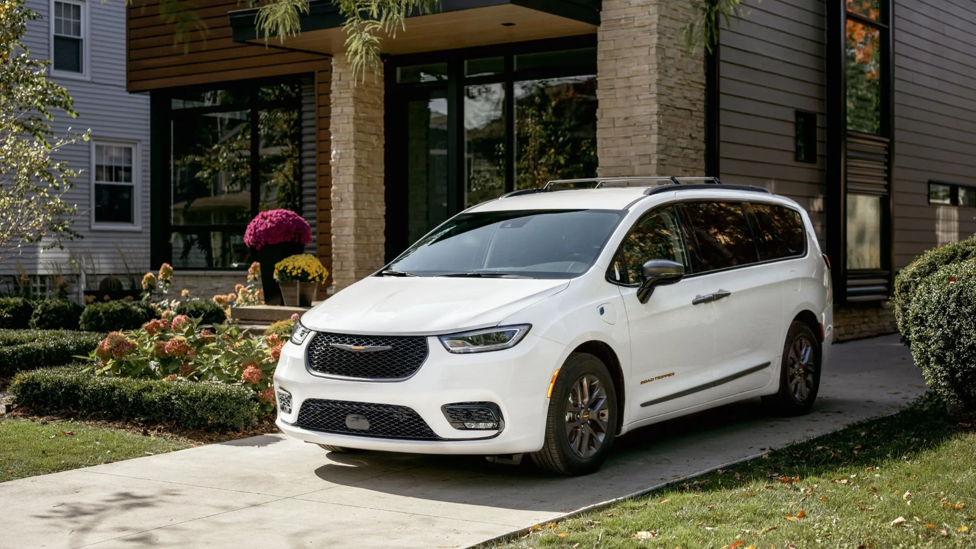 Góc ba phần tư phía trước của Chrysler Pacifica 2023 màu trắng đỗ trên đường lái xe, thể hiện thiết kế sang trọng và kích thước lớn của xe.