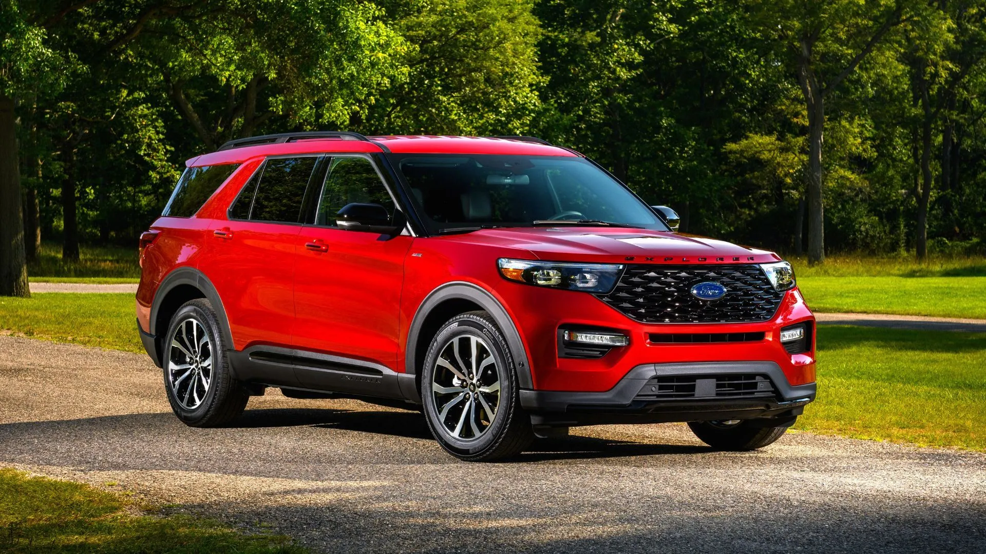 Góc ba phần tư phía trước của Ford Explorer 2022 ST-Line màu đỏ đỗ trên sỏi với cây cối phía sau, thể hiện sự mạnh mẽ và sang trọng.