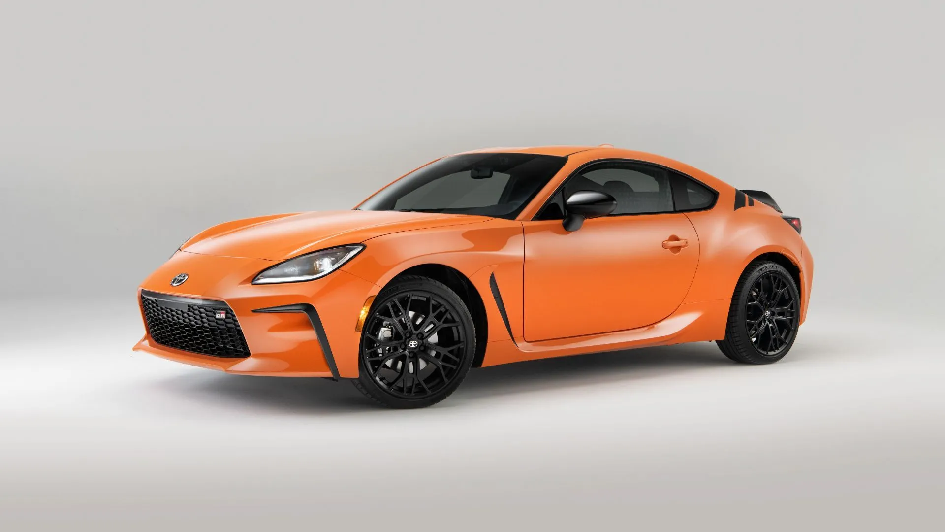 Góc tĩnh ba phần tư phía trước của một chiếc Toyota GR86 Special Edition 2023 màu cam trong studio với nền sáng.