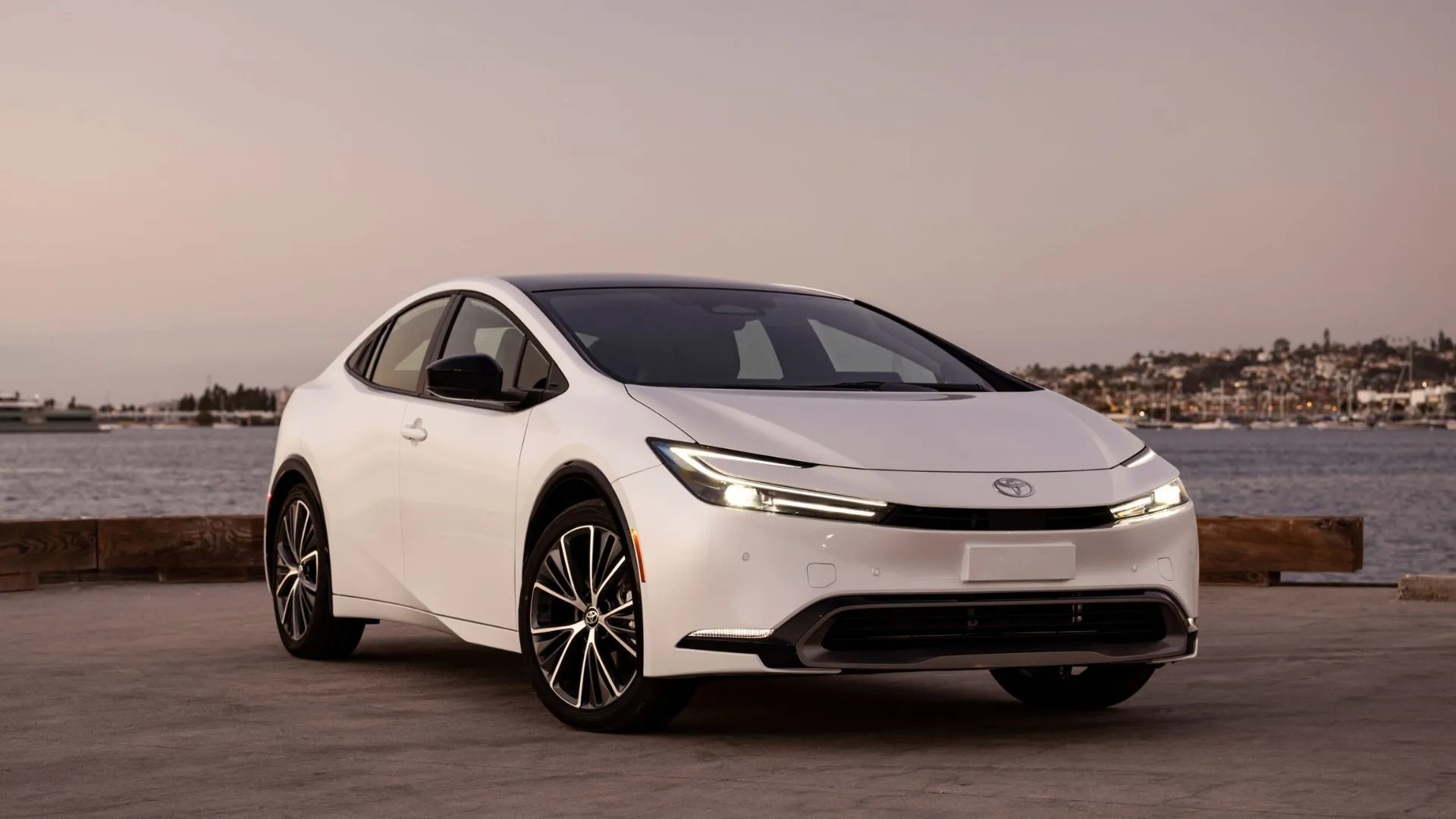 Góc tĩnh ba phần tư phía trước của một chiếc Toyota Prius Limited 2025 màu trắng đỗ với đại dương phía sau.