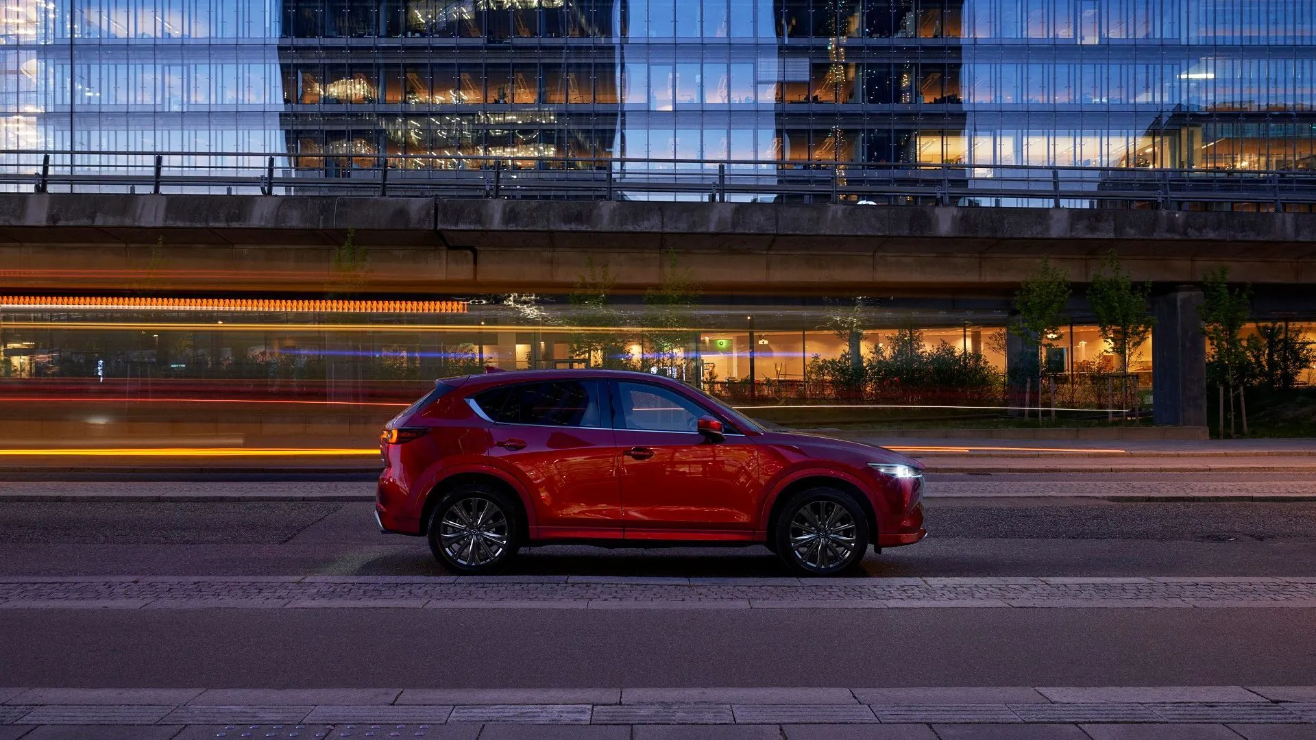 Hình ảnh bên hông Mazda CX-5 màu đỏ lướt qua thành phố về đêm, minh họa thiết kế Kodo đặc trưng của Mazda