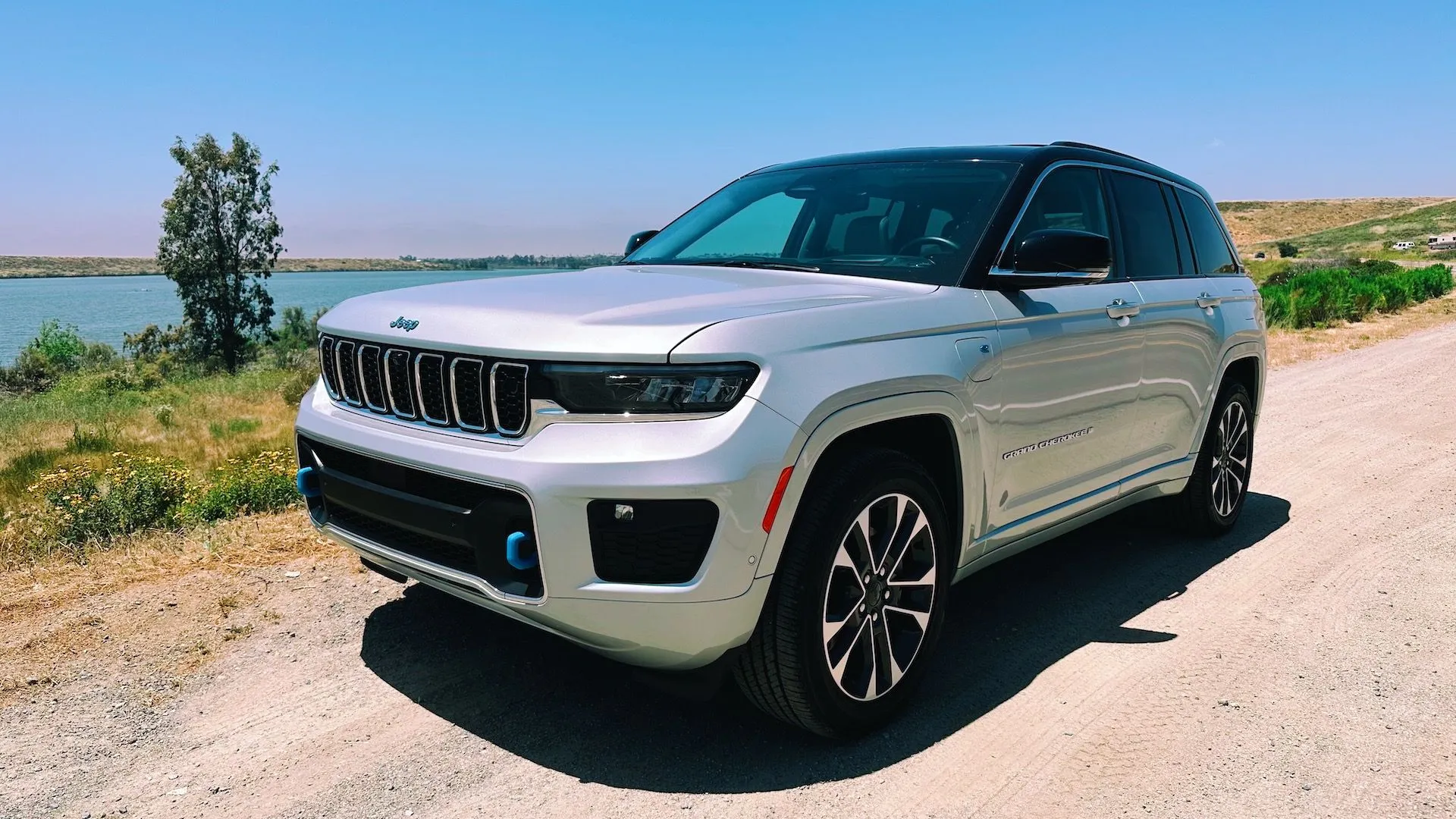 Hình ảnh góc 3/4 phía trước của một chiếc Jeep Grand Cherokee Overland 4xe màu bạc đang đỗ bên bờ hồ, thể hiện sự mạnh mẽ và sang trọng của dòng SUV hybrid.