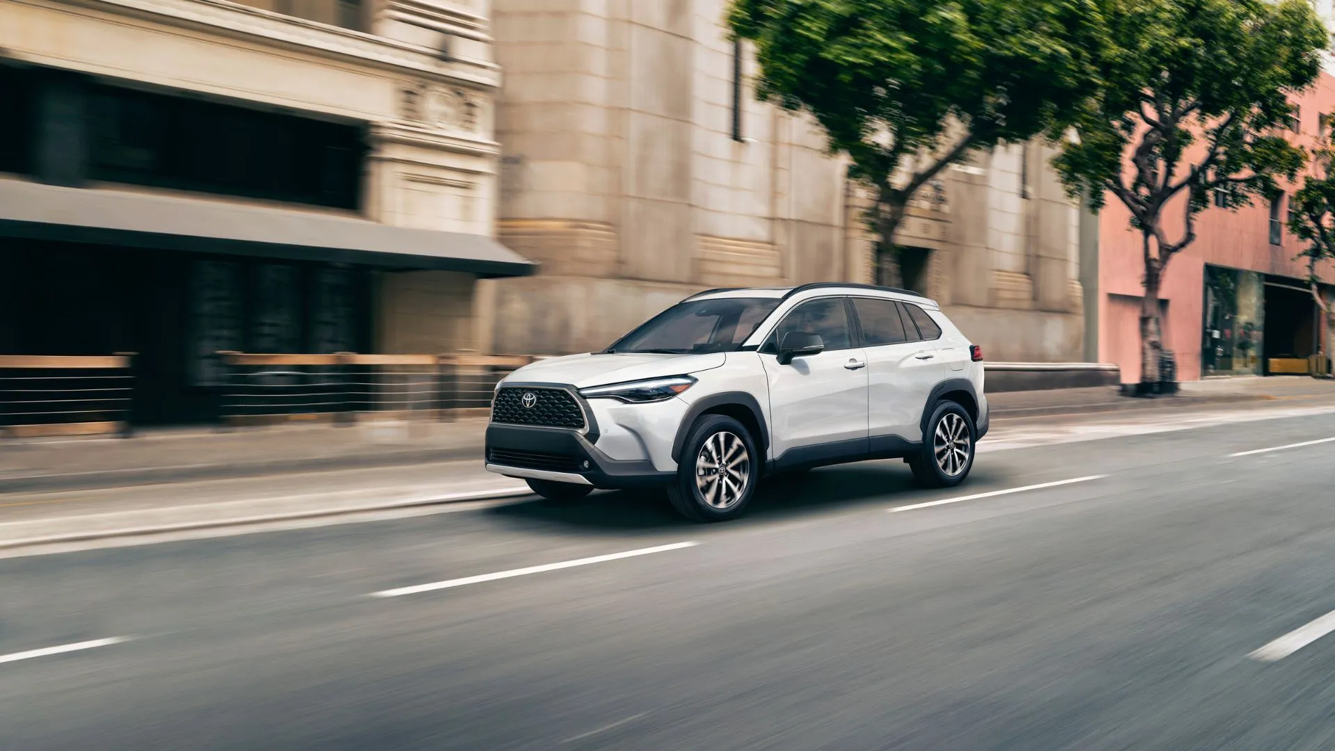 Hình ảnh góc 3/4 phía trước động của Toyota Corolla Cross Hybrid XSE 2025 màu trắng ngọc trai đang di chuyển trong thành phố, thể hiện sự nhỏ gọn và tiện lợi.