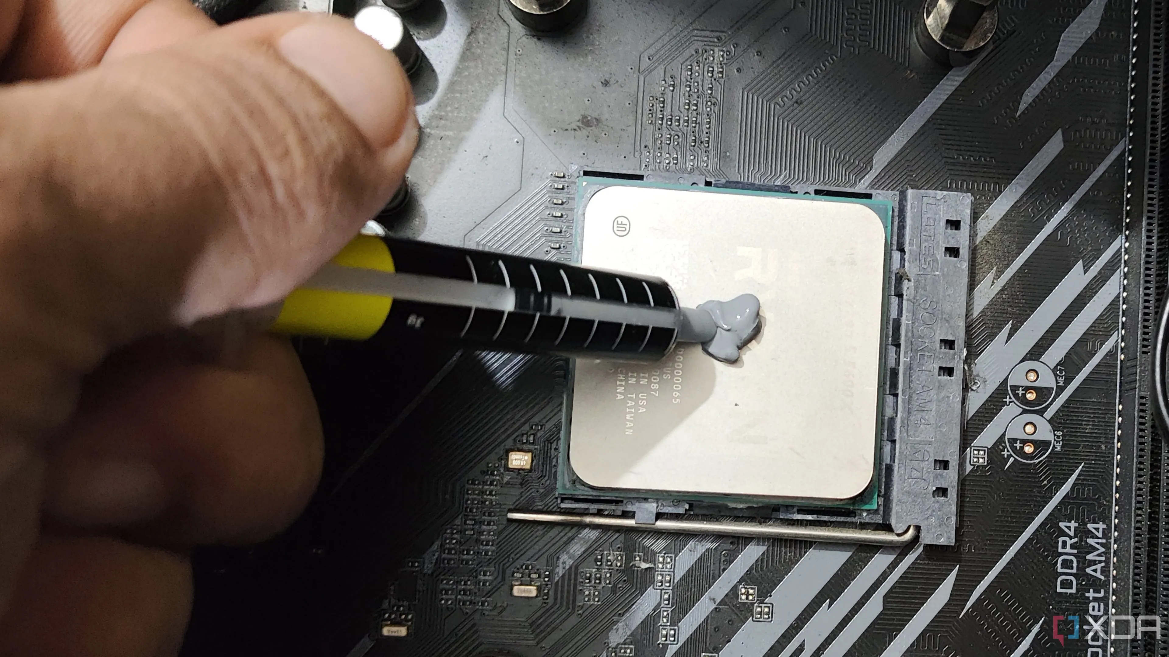Hình ảnh một người đang bôi keo tản nhiệt lên bề mặt CPU AMD Ryzen 5 5600X, quy trình quan trọng để duy trì nhiệt độ ổn định cho linh kiện.