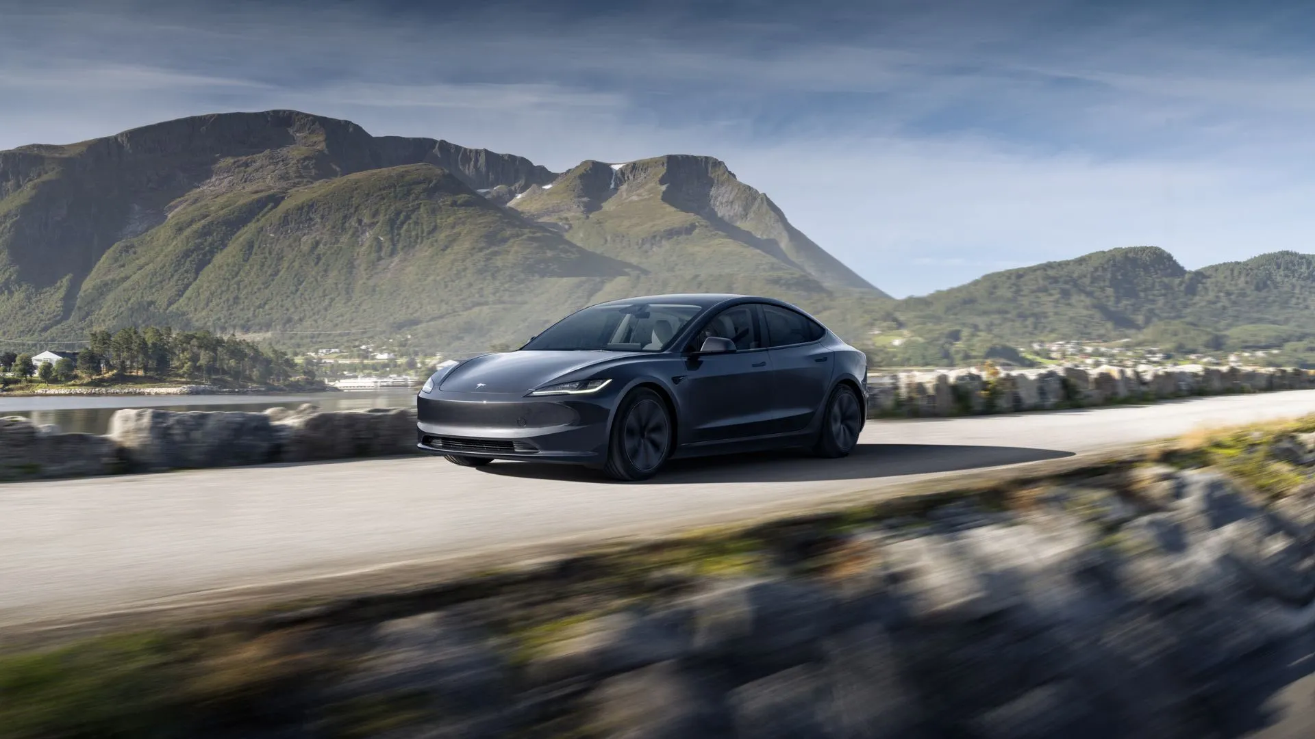 Hình ảnh năng động góc 3/4 phía trước của chiếc Tesla Model 3 màu xám với khung cảnh núi non hùng vĩ phía sau.