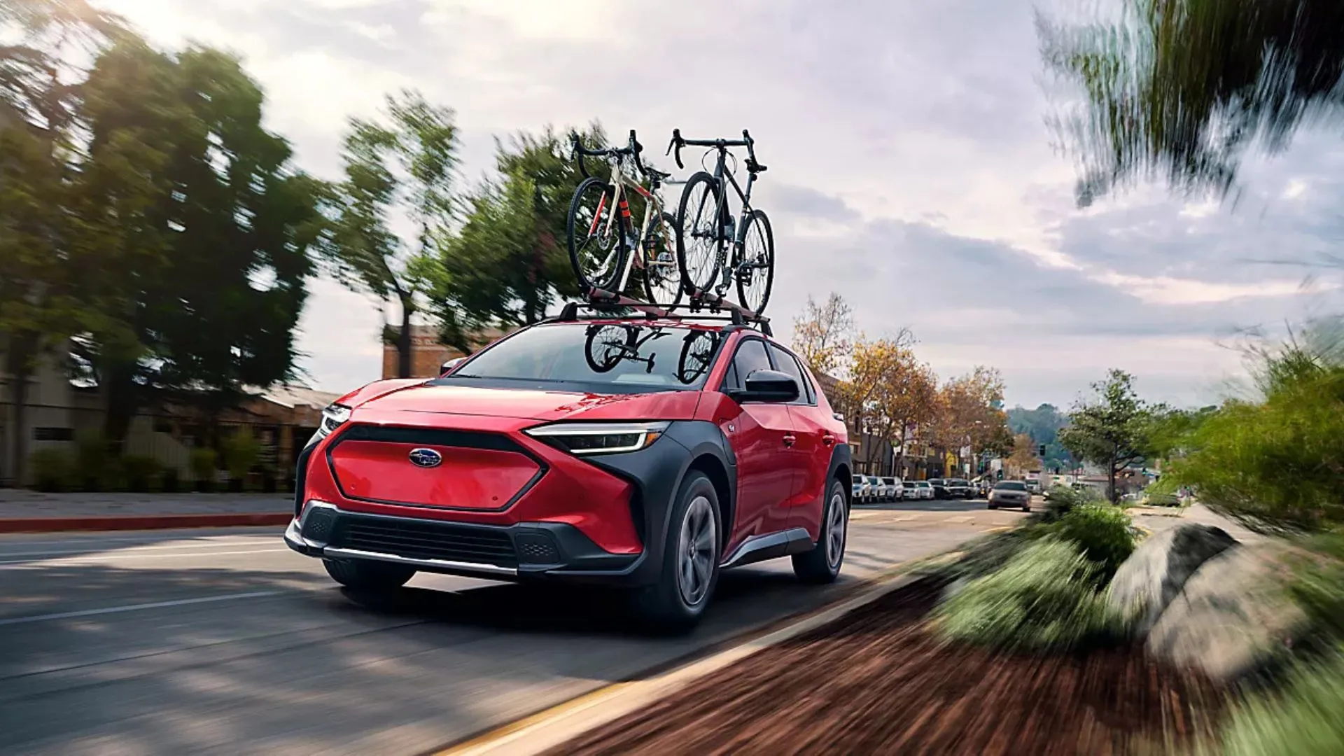 Hình ảnh xe Subaru Solterra 2025 màu đỏ đang di chuyển trên đường nông thôn, có gắn xe đạp trên nóc.