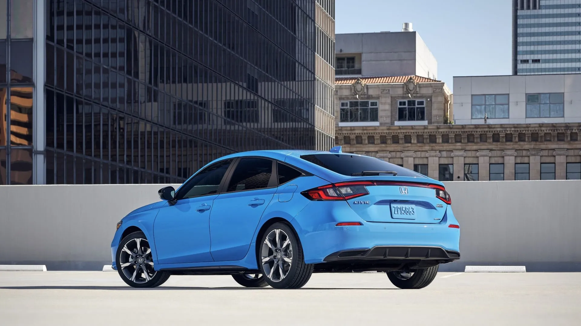 Honda Civic Hatchback 2025 màu xanh đậu trên sân thượng, bối cảnh đô thị hiện đại, góc nhìn từ phía sau