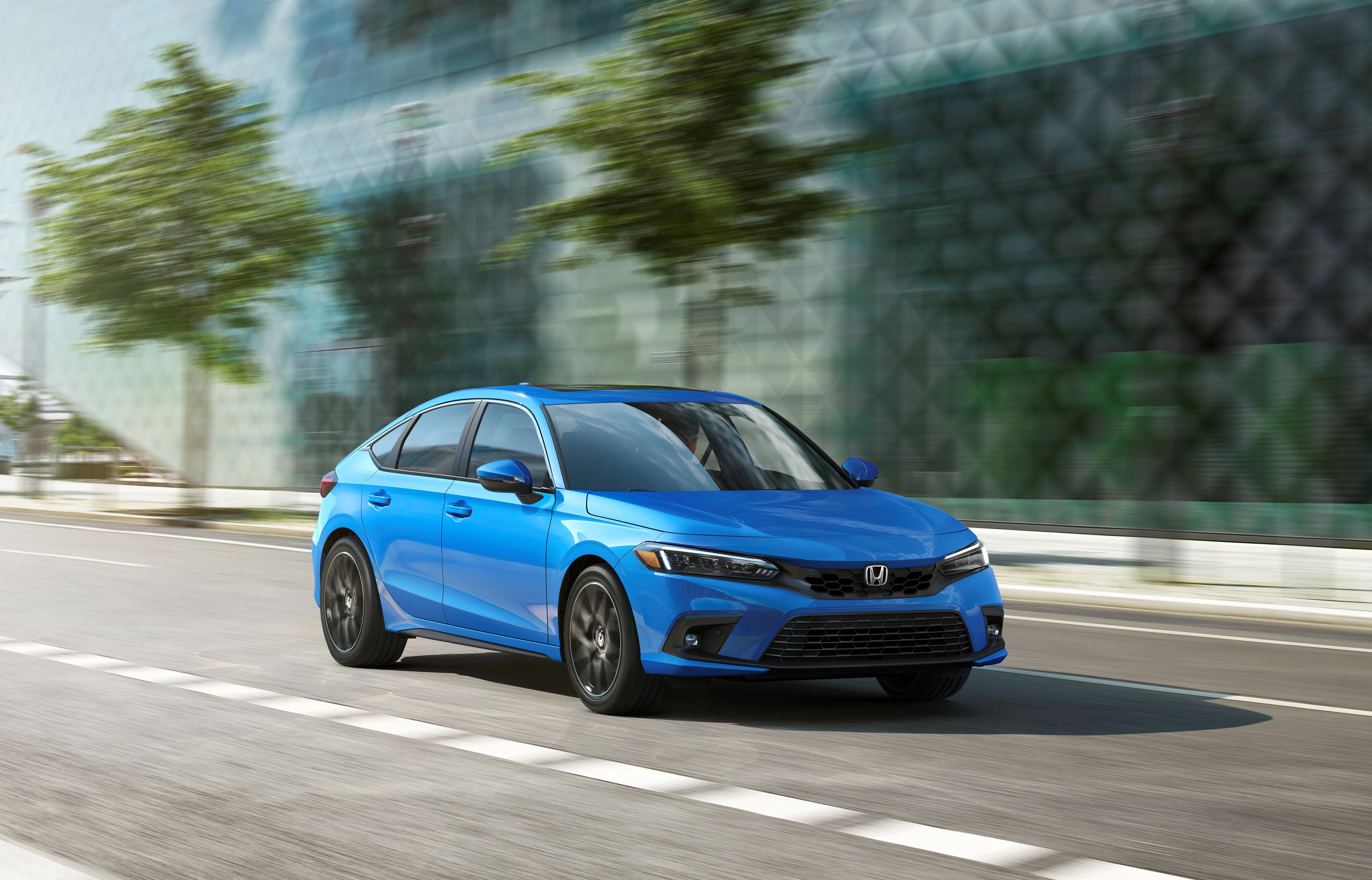 Honda Civic Hatchback màu xanh ngọc di chuyển trên đường phố, thể hiện sự linh hoạt và hiện đại