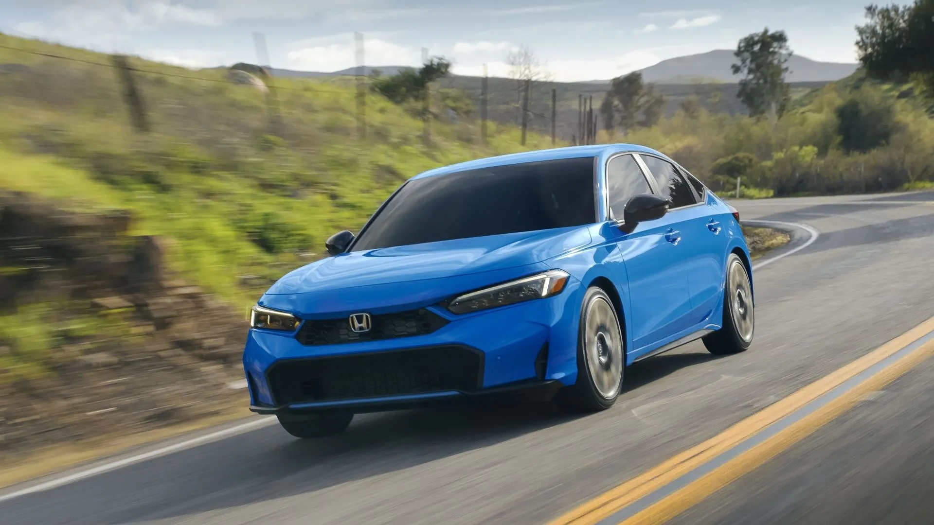 Honda Civic Hatchback Sport Touring Hybrid 2025 màu xanh ngọc di chuyển trên đường, nổi bật với thiết kế hiện đại và giá trị vượt trội