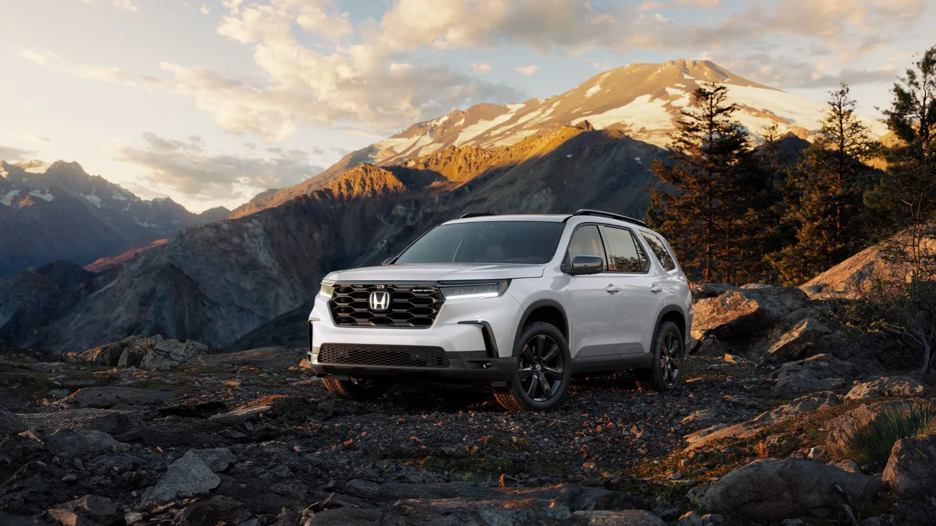Honda Pilot Black Edition 2025 màu trắng đỗ trong rừng với núi non phía sau, biểu trưng cho SUV gia đình bền bỉ.