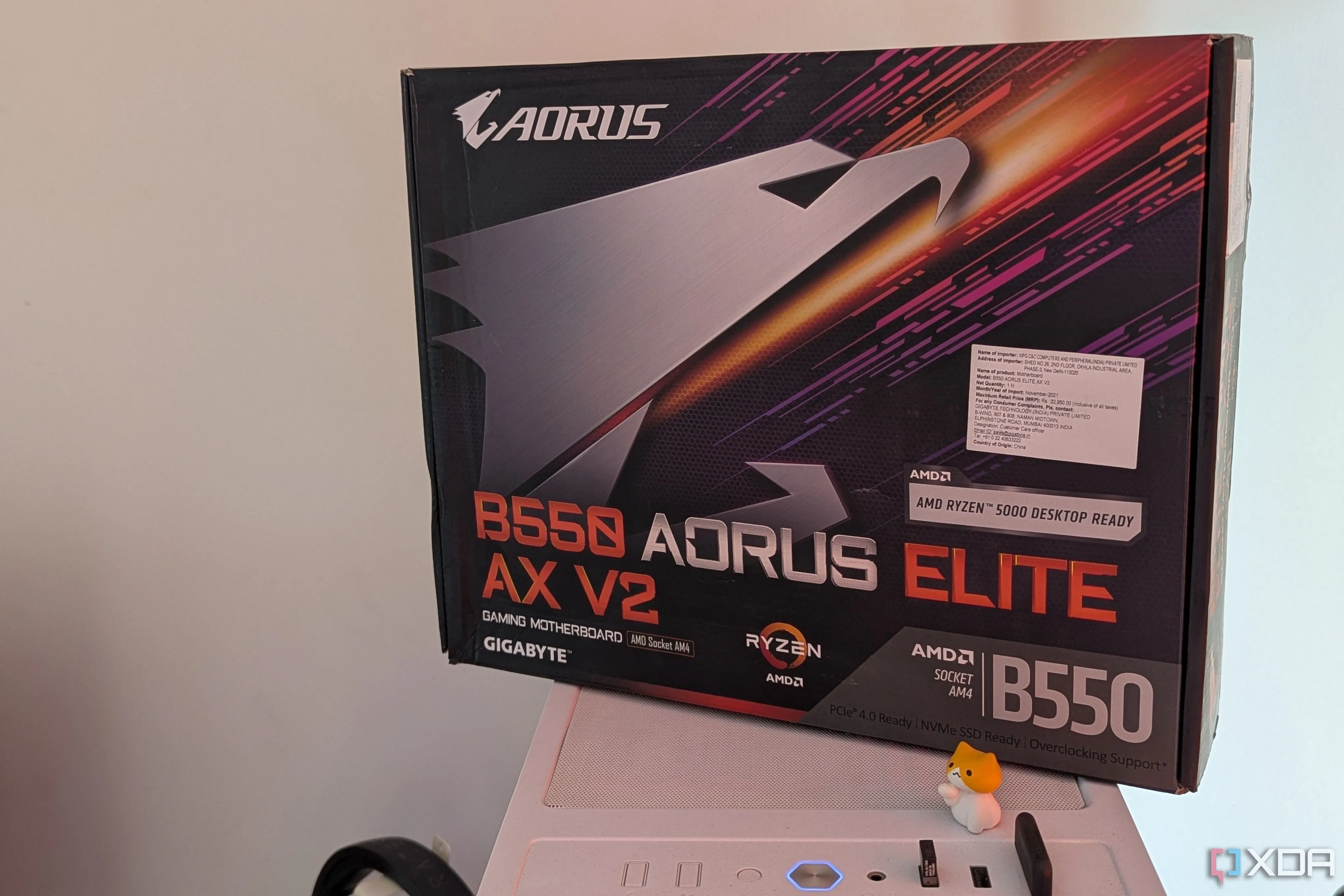Hộp bo mạch chủ Gigabyte B550 Aorus Elite AX V2 đặt trên một vỏ case PC màu trắng, thể hiện yếu tố thẩm mỹ của linh kiện