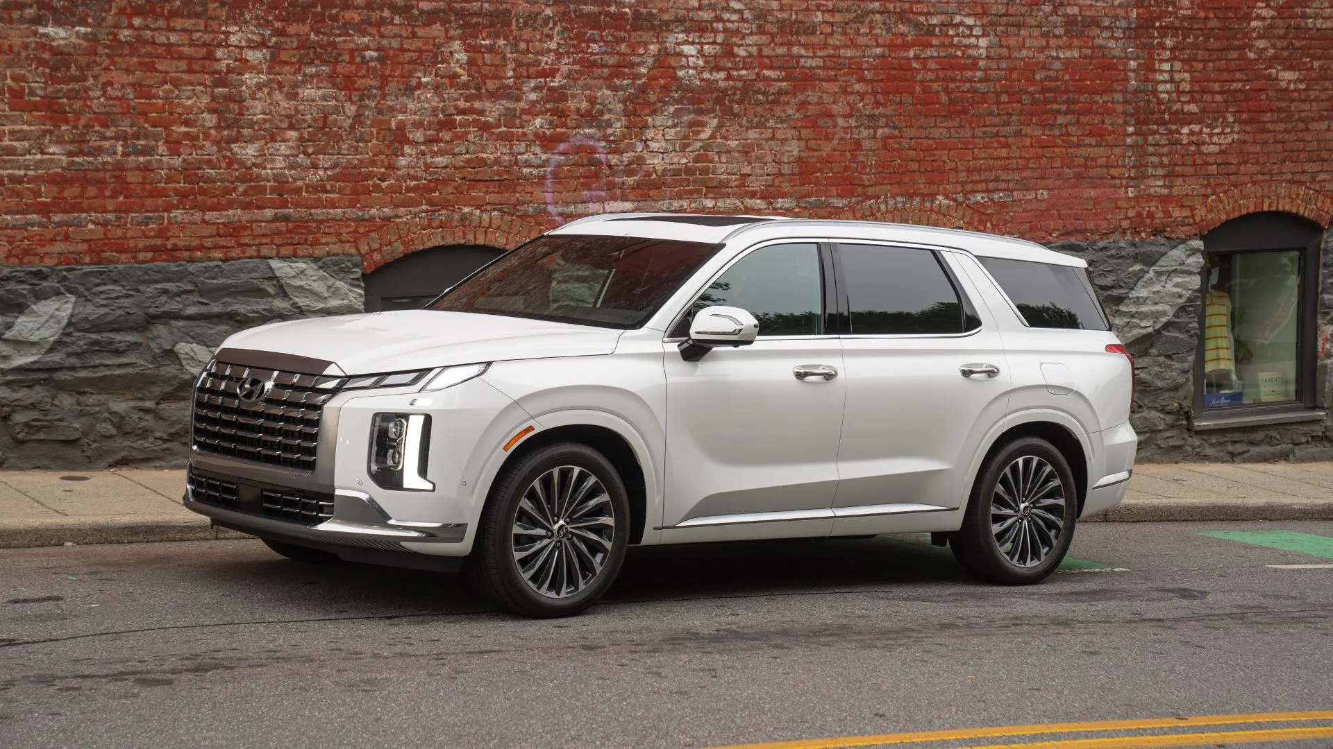Hyundai Palisade 2025 màu trắng đậu cạnh vỉa hè với bức tường gạch vẽ graffiti