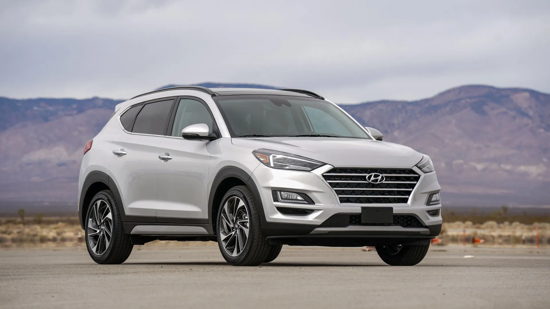 Hyundai Tucson Hybrid 2021 màu bạc đậu trên đường nhựa với núi non phía sau.