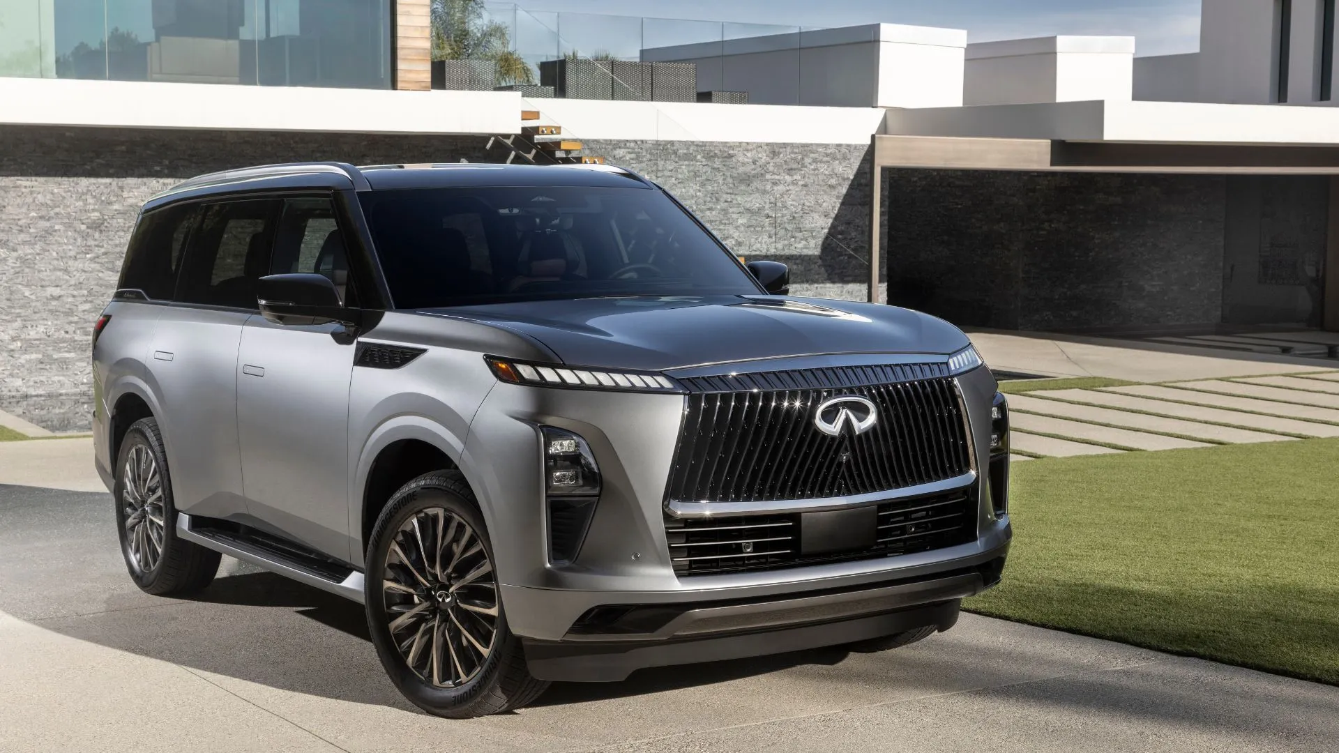 Infiniti QX80 2025 màu xám bạc với thiết kế sang trọng, hiện đại, đang đỗ trước một căn nhà, cho thấy khả năng kéo ấn tượng của SUV hạng sang này